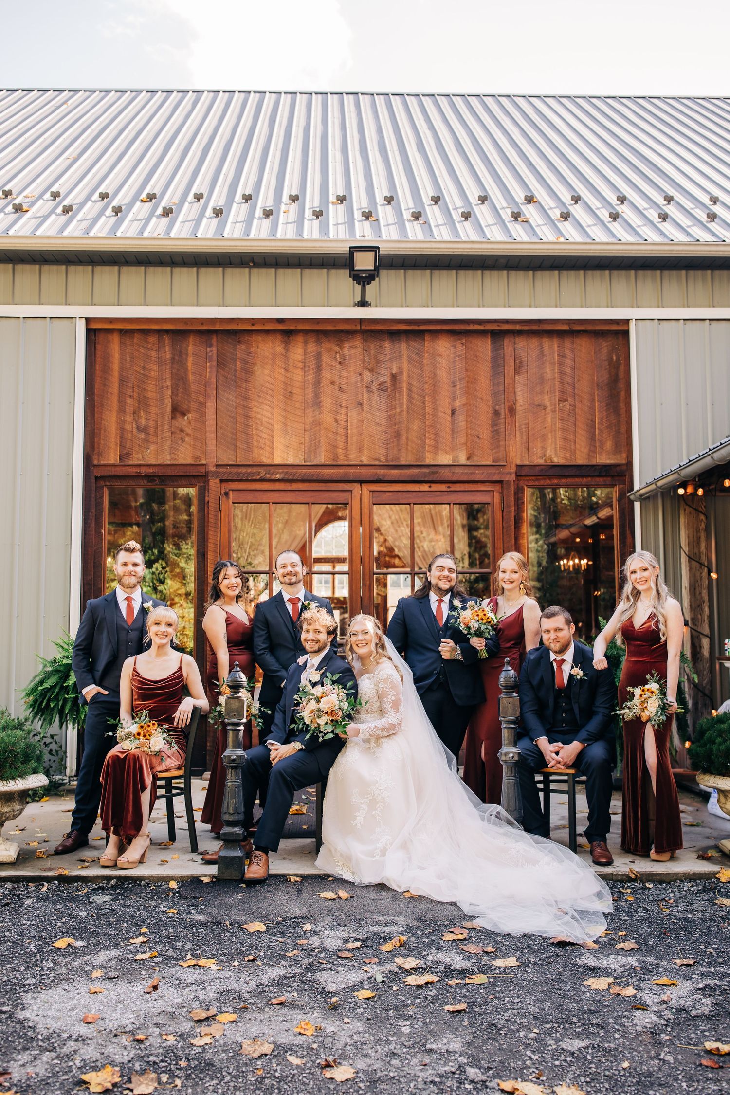 Wedding party posed in front of rustic barn venue with burgundy and white color scheme.