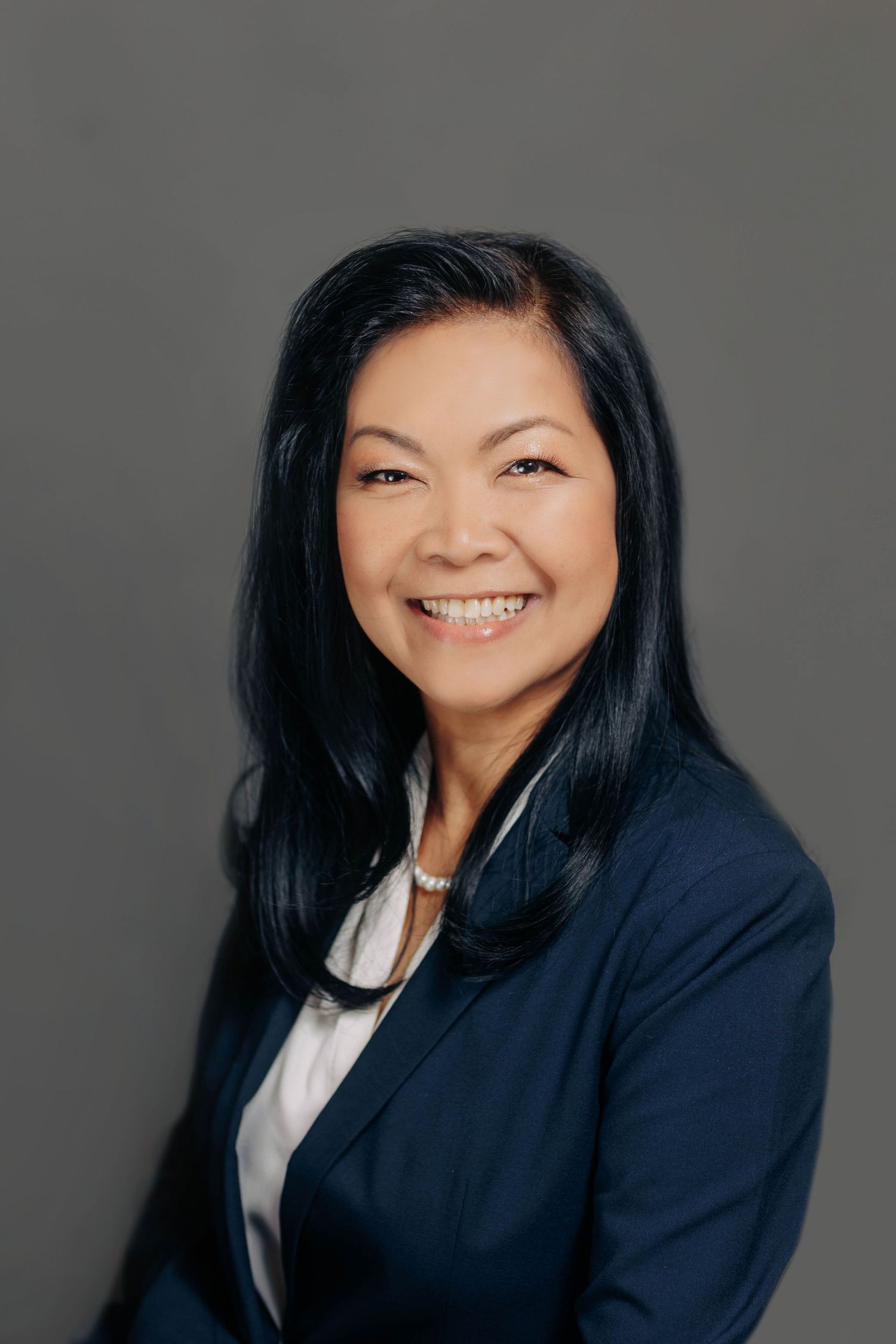 Professional business portrait with warm genuine smile against dark backdrop.