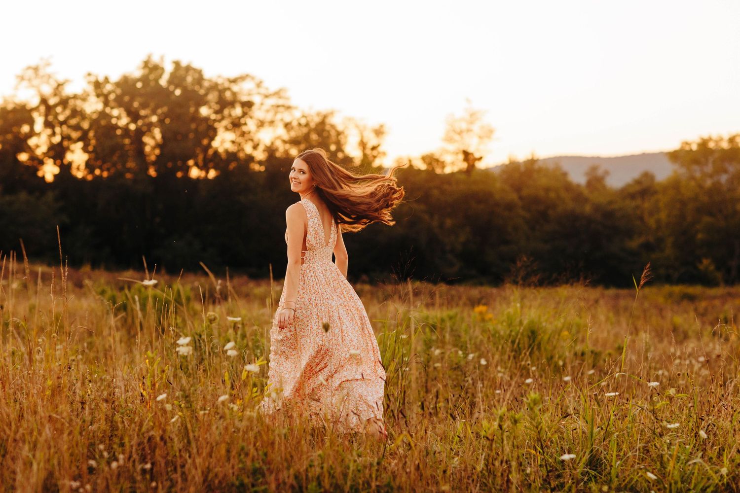 A woman in a white dress dances gracefully in a golden field at sunset.