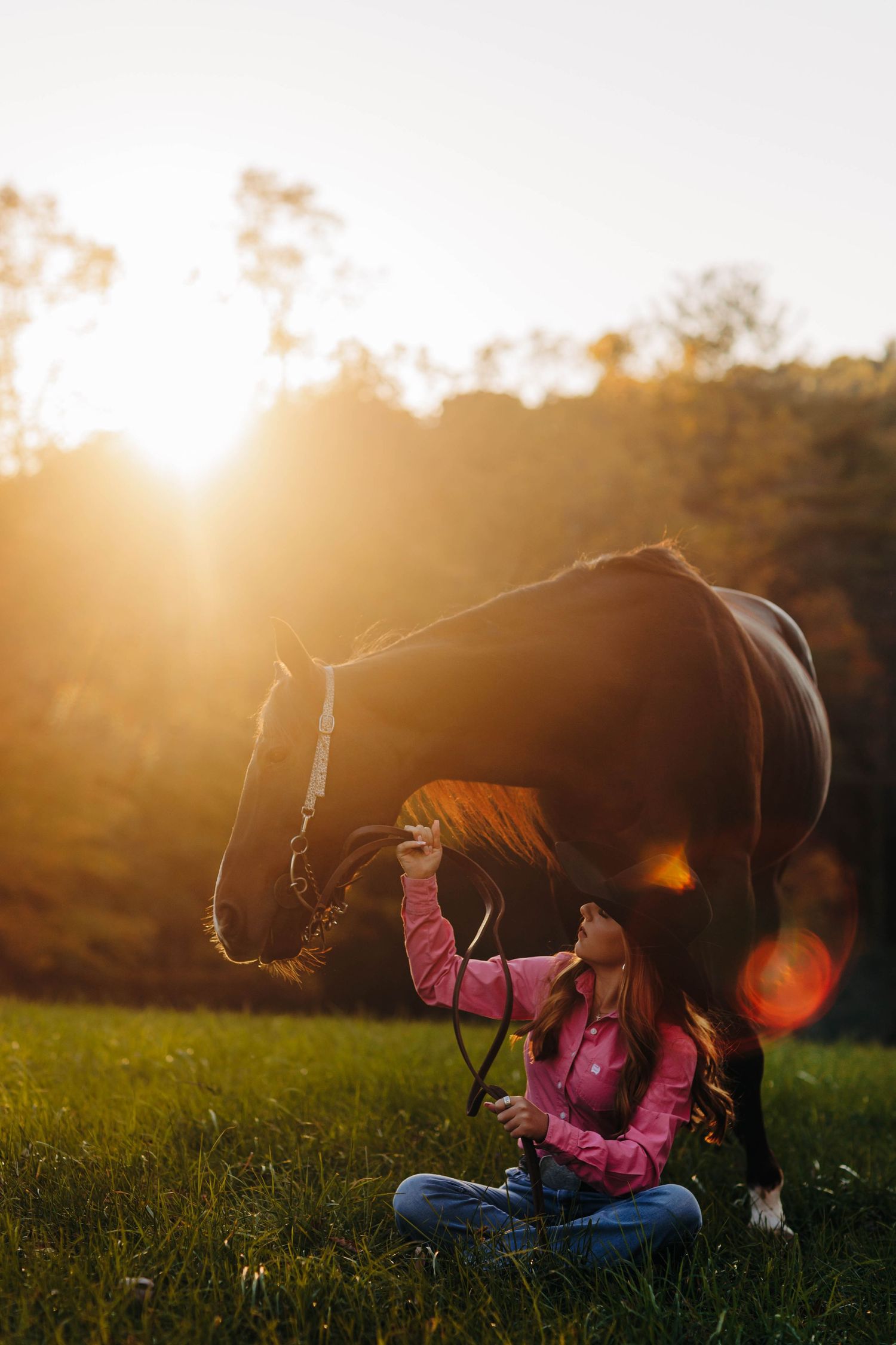 Silhouette of someone in a pink jacket sitting in a grassy field at sunset.
