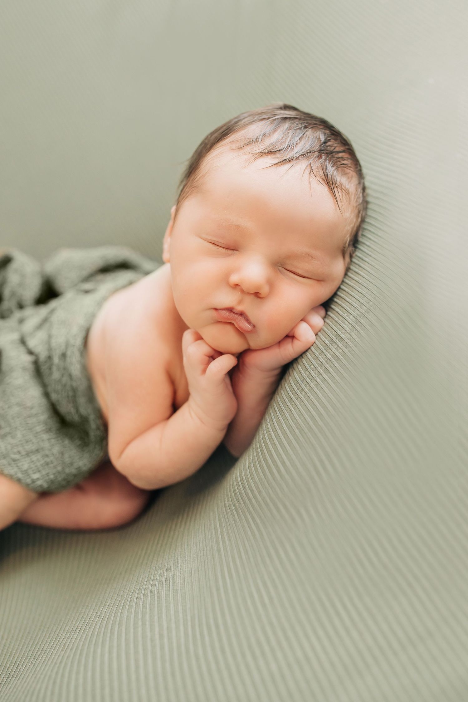 Peaceful sleeping newborn baby in grey outfit on textured grey surface.