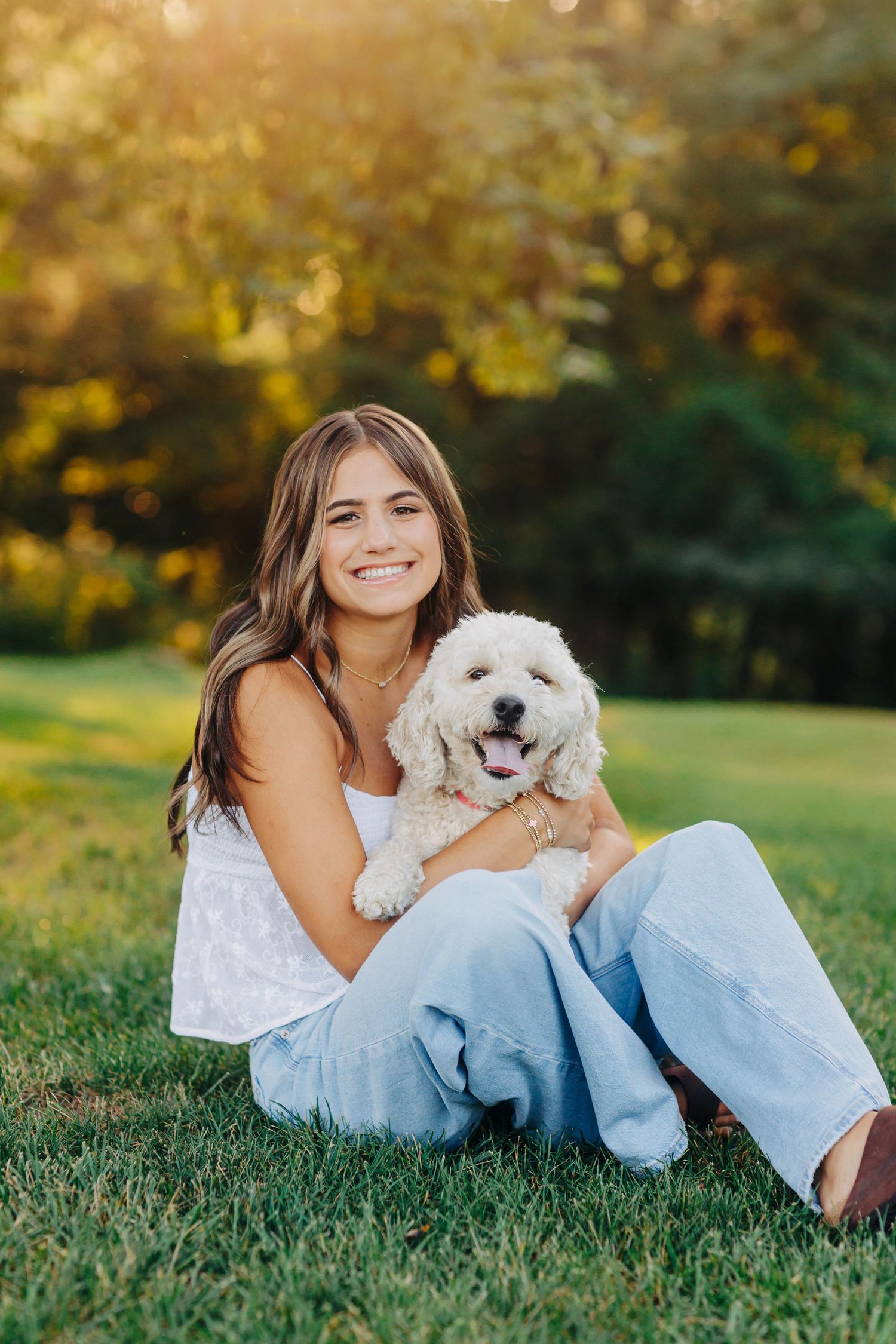 Person sitting on grass holding happy white fluffy dog in summer setting.