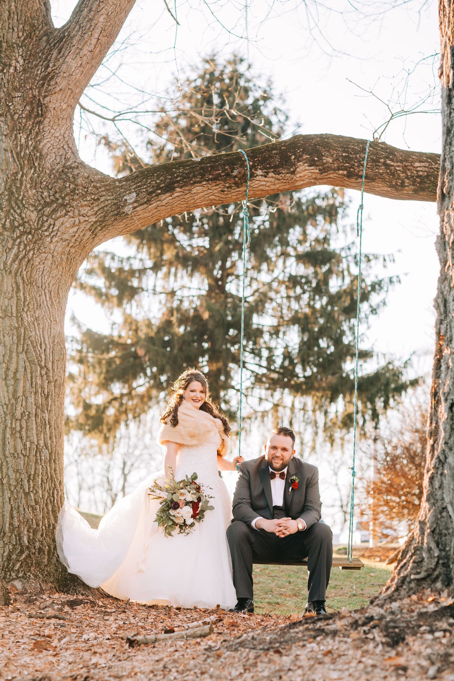 A romantic autumn wedding photoshoot under large trees with fallen leaves.