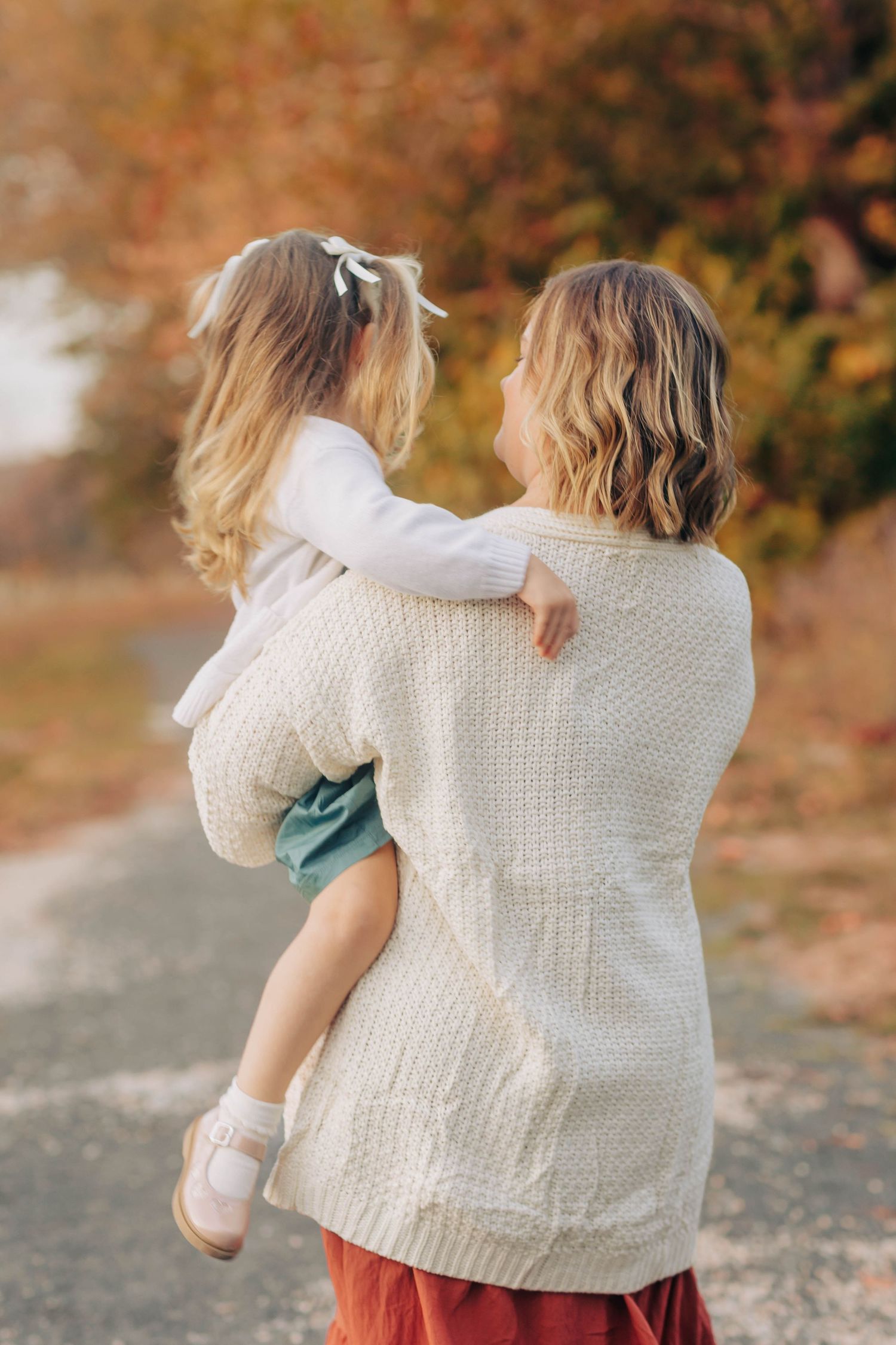 Back view of person in white knit sweater walking during fall season.