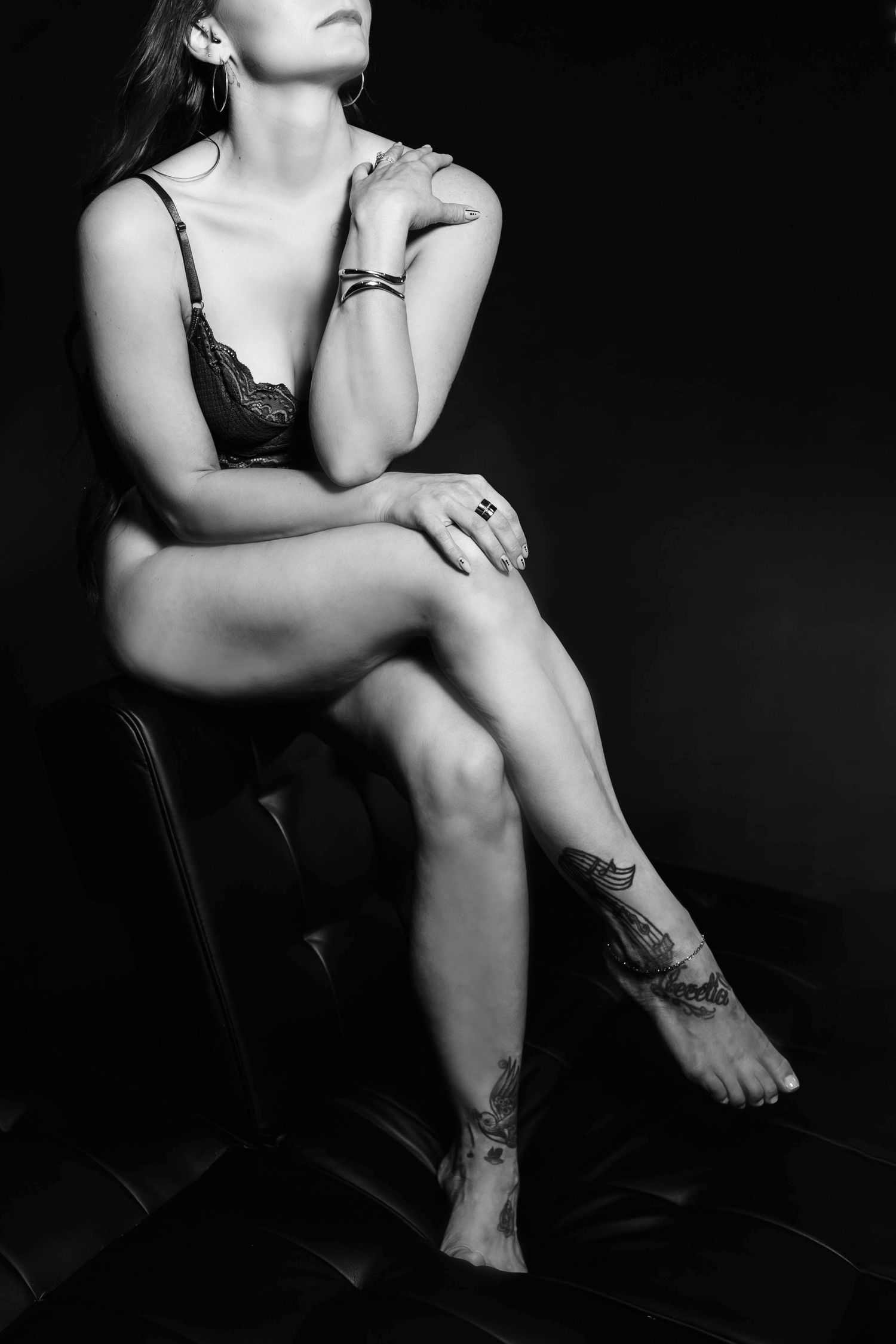 Artistic black and white portrait showing legs and tattoos in moody lighting.