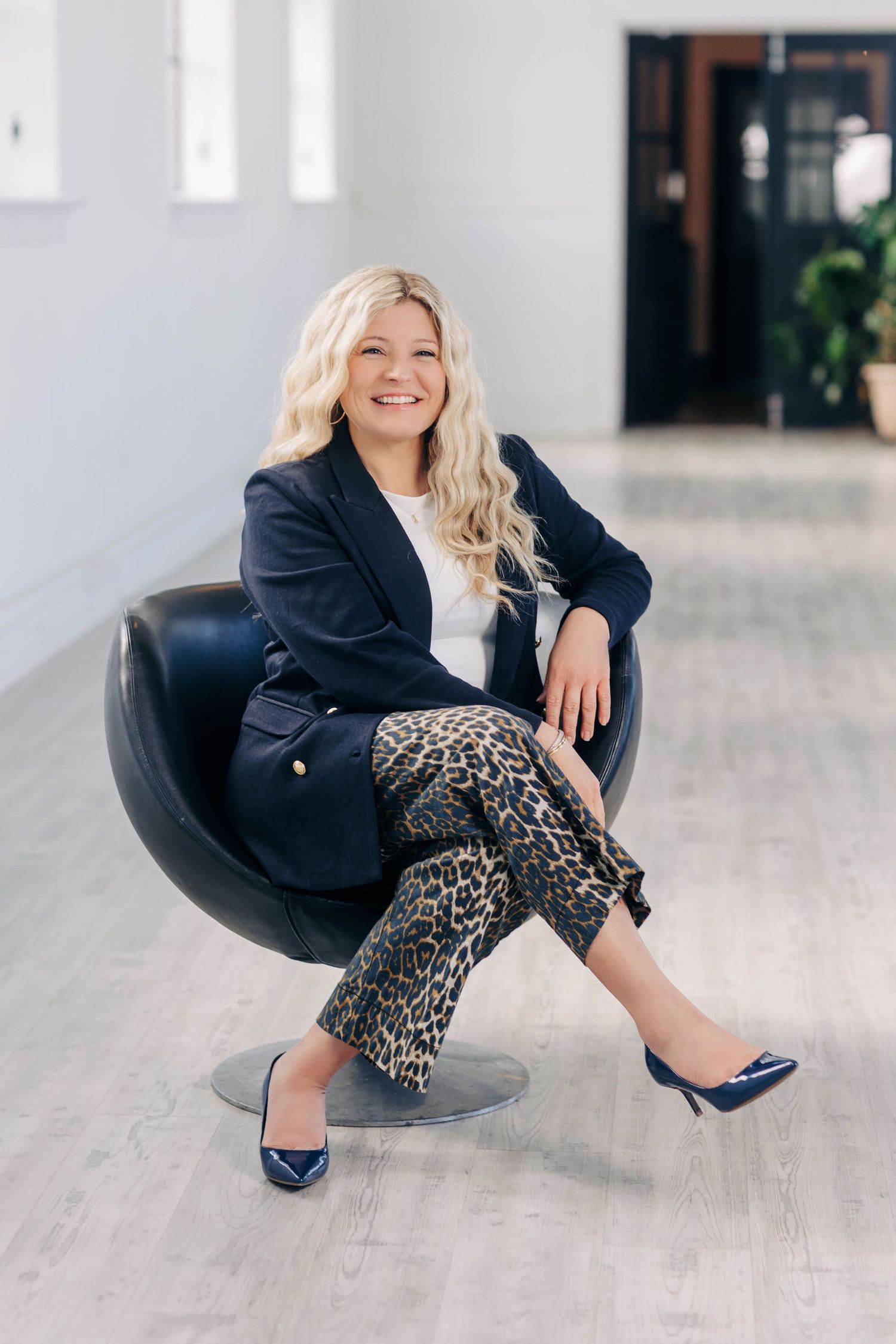 Fashion shots of person in black blazer and leopard pants posing playfully in modern space.