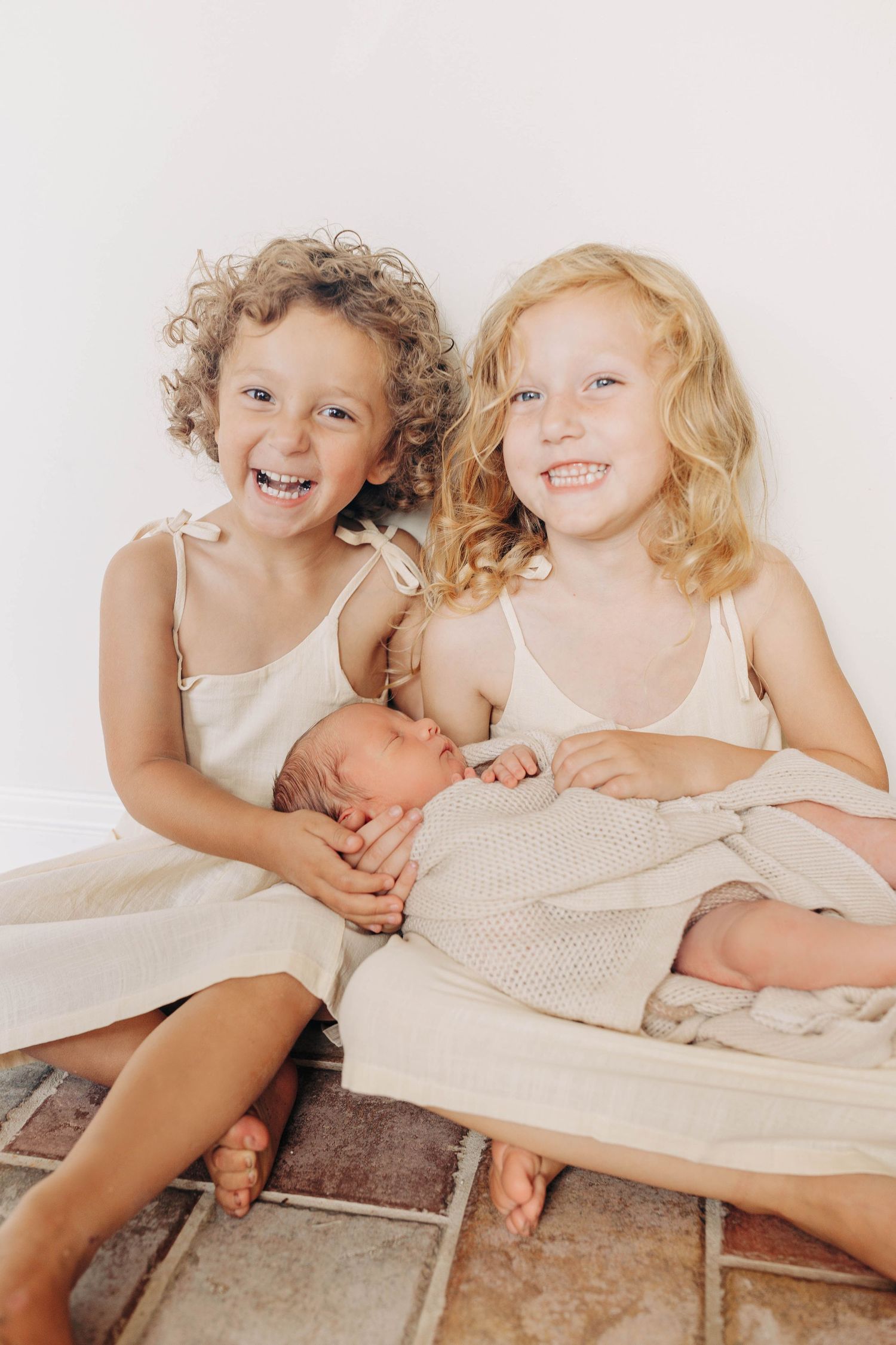Two children in light clothing sitting together with a newborn.