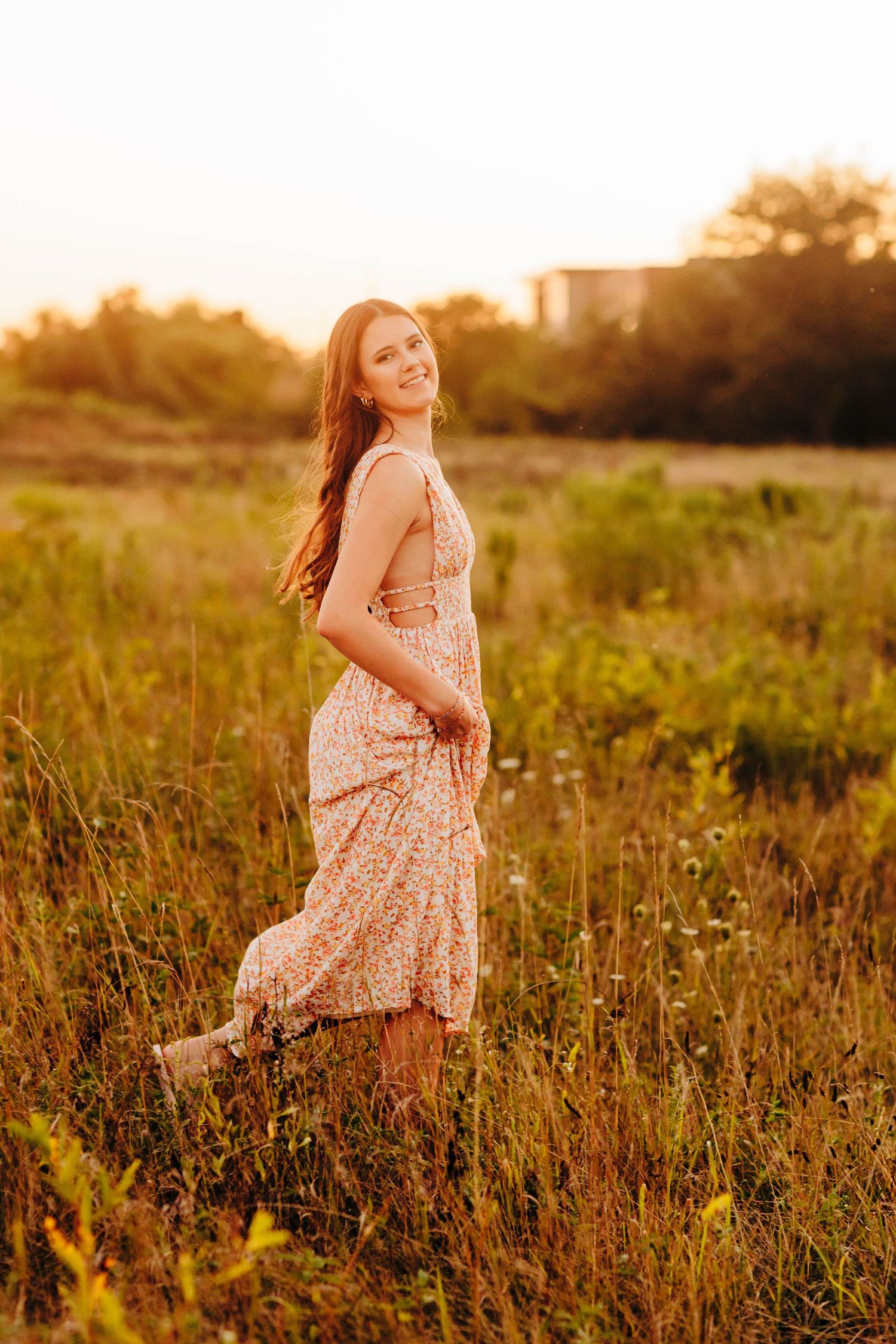 Flowing floral dress catches evening light in tall grass meadow.
