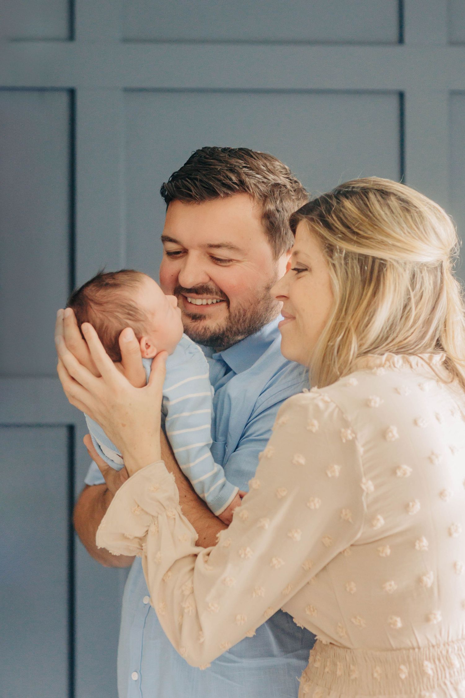 Family sharing intimate moment with newborn baby against blue wall.