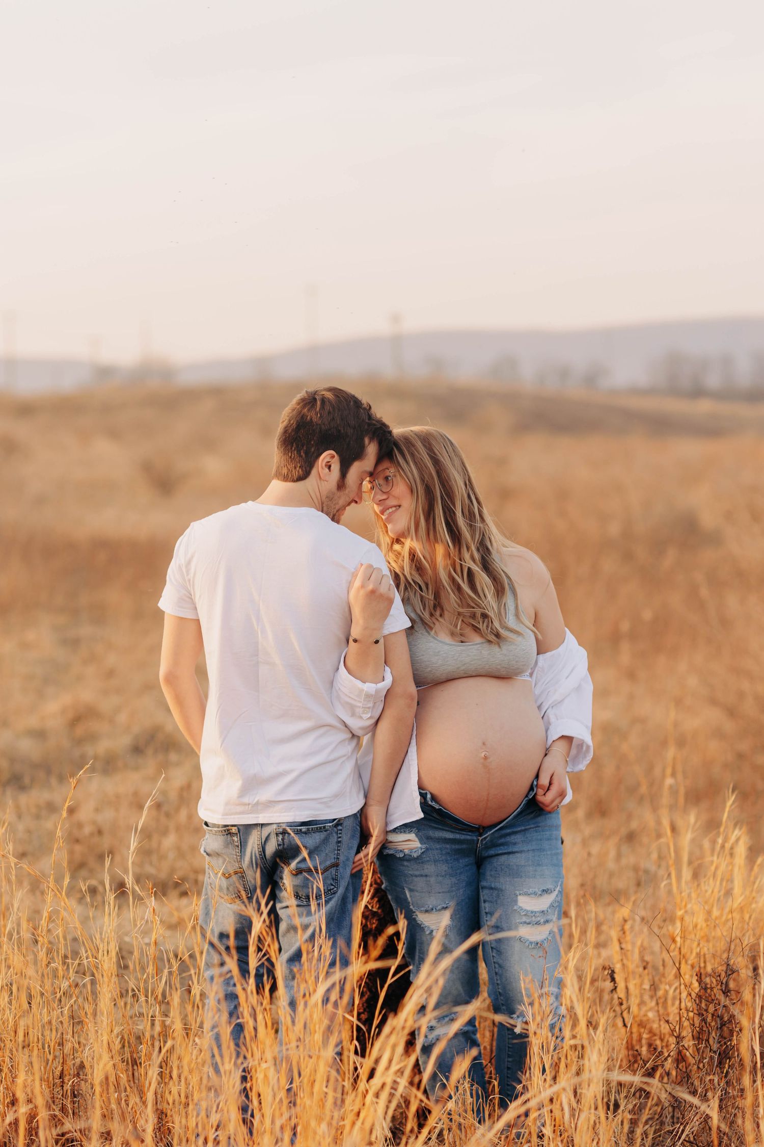 Couple embracing in golden field during sunset maternity photoshoot.