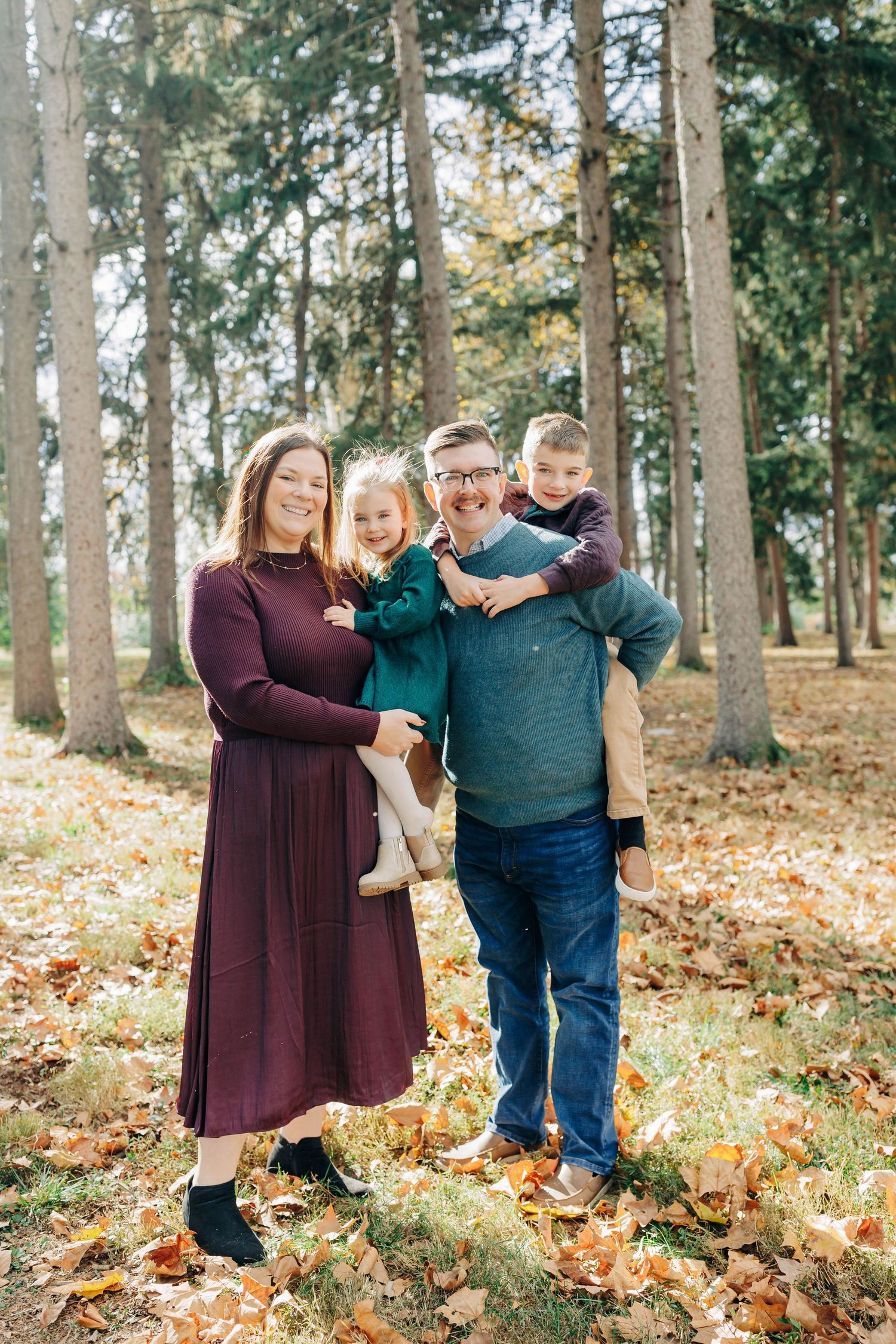Family autumn portrait session among tall trees with fallen leaves.