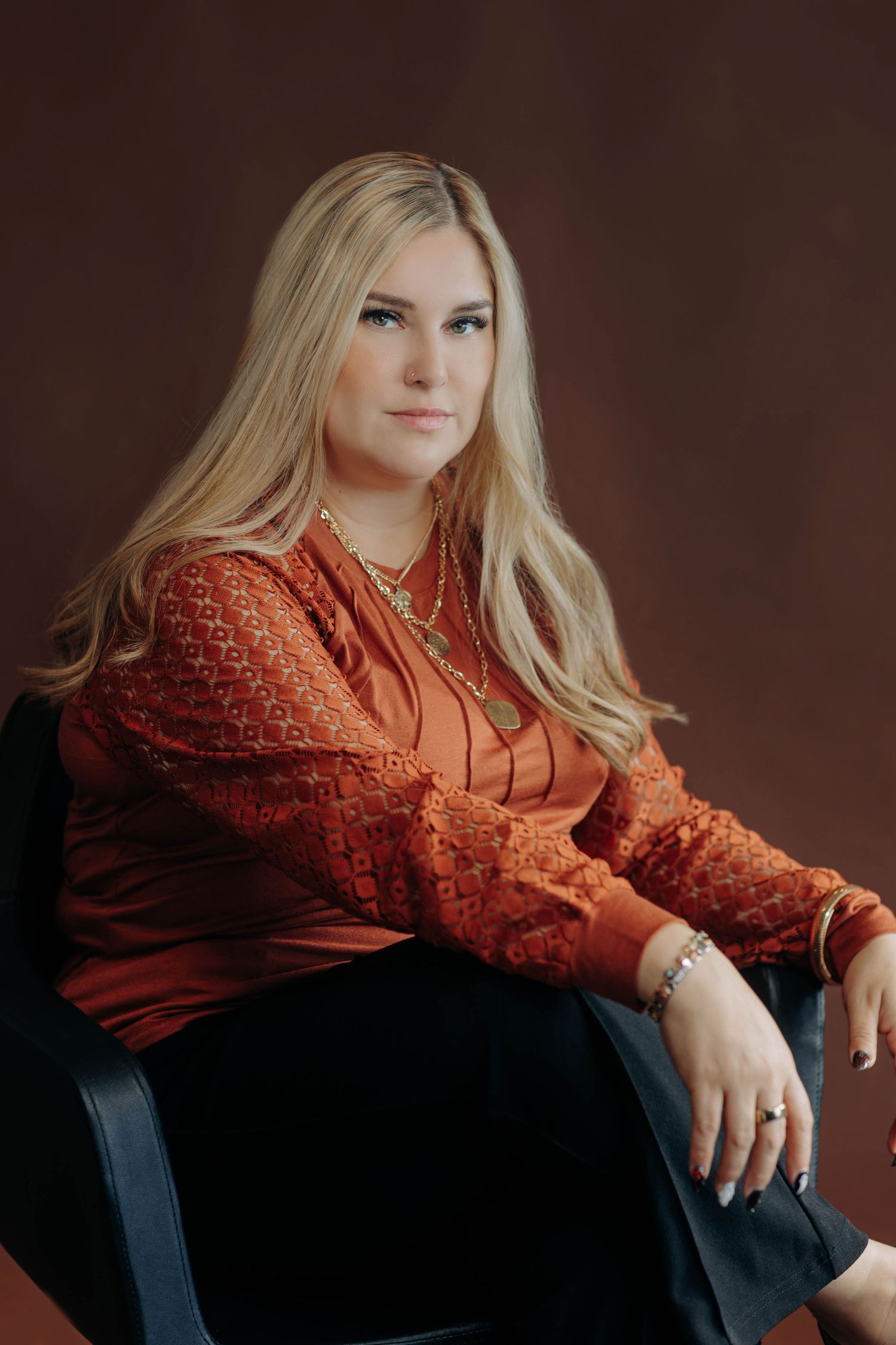 A woman reclines on dark furniture wearing an orange lace top and dark pants.