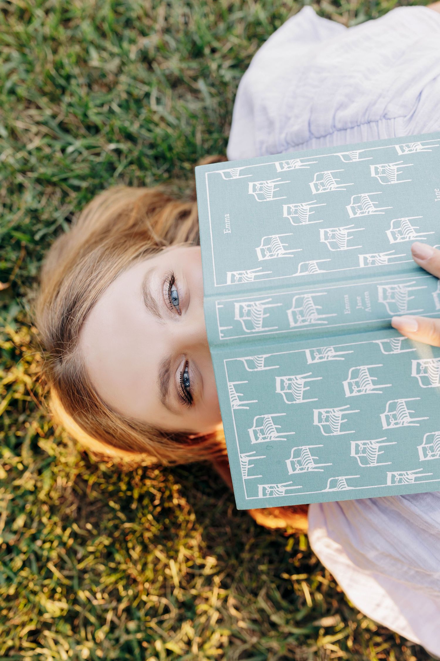 Person lying on grass holding a mint green book with musical notes.