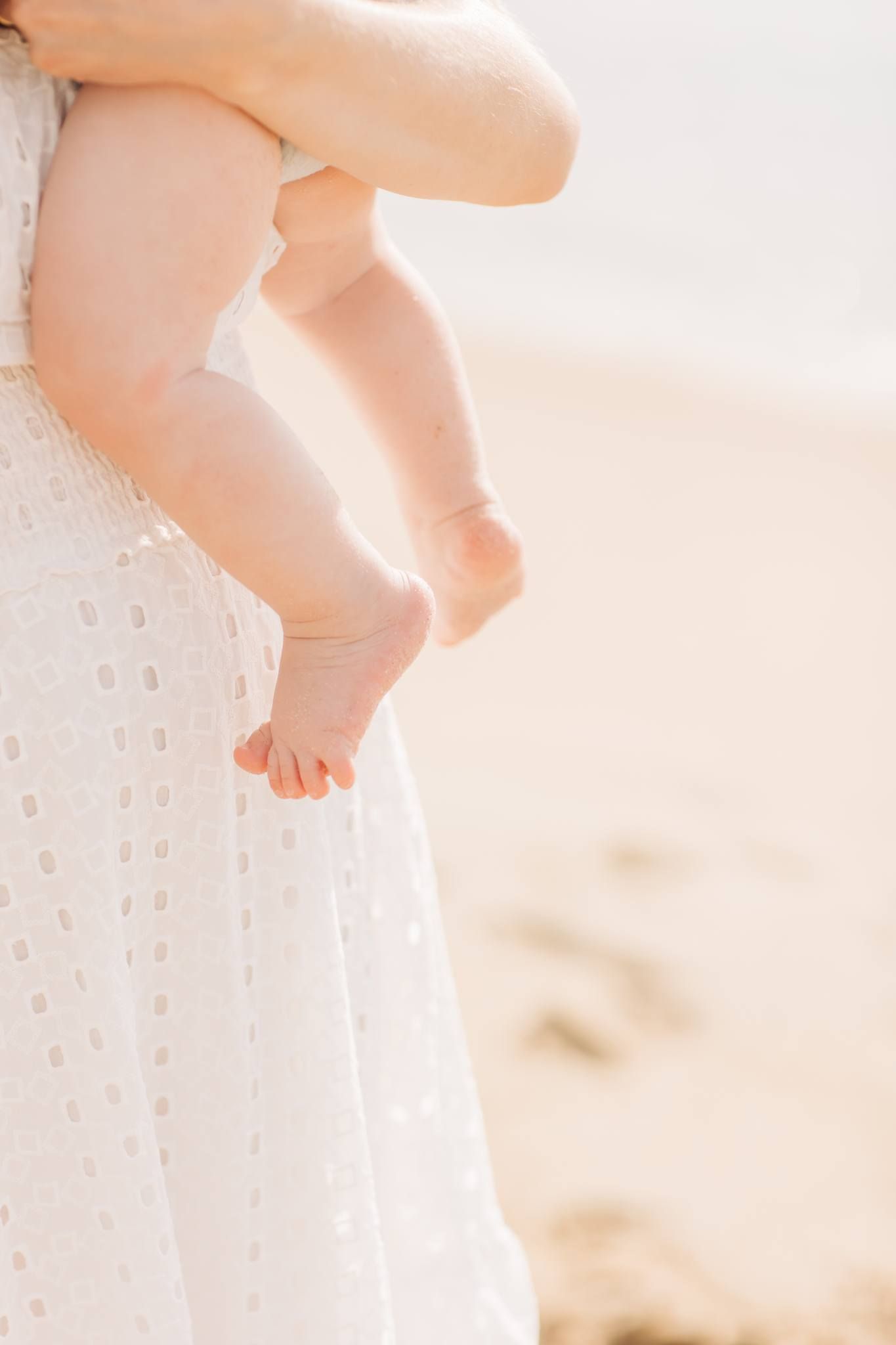 Close up of baby feet against a white eyelet dress in soft natural light.