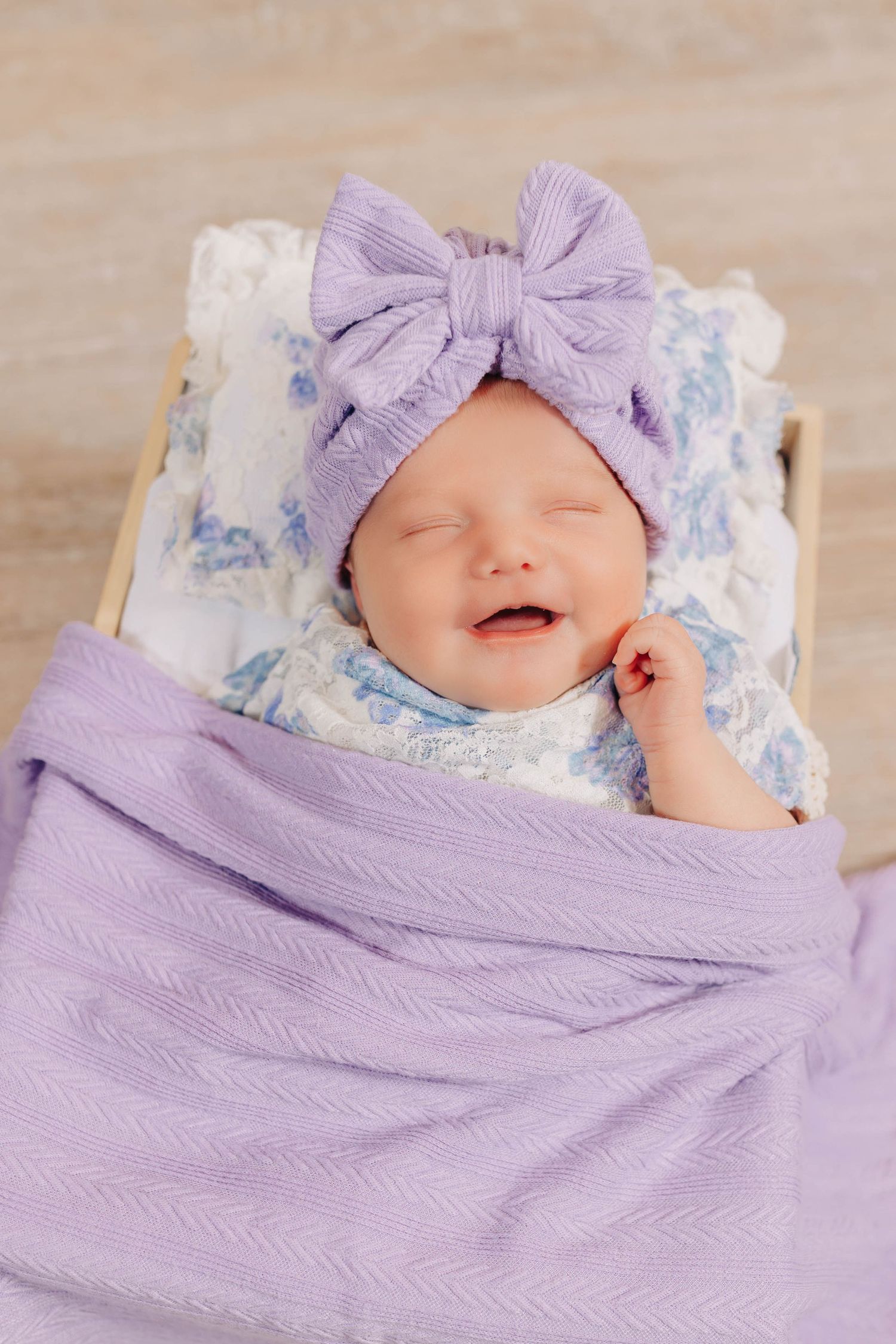 Newborn baby wrapped in soft purple blanket with matching bow headband sleeping peacefully.