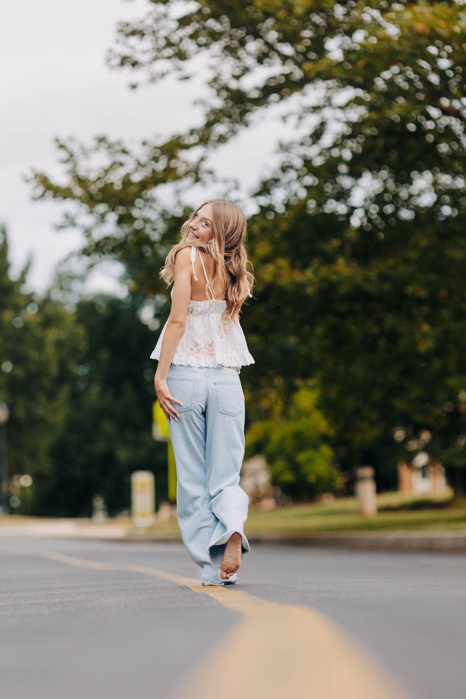 Person in light top and jeans walking down an empty street on a summer day.