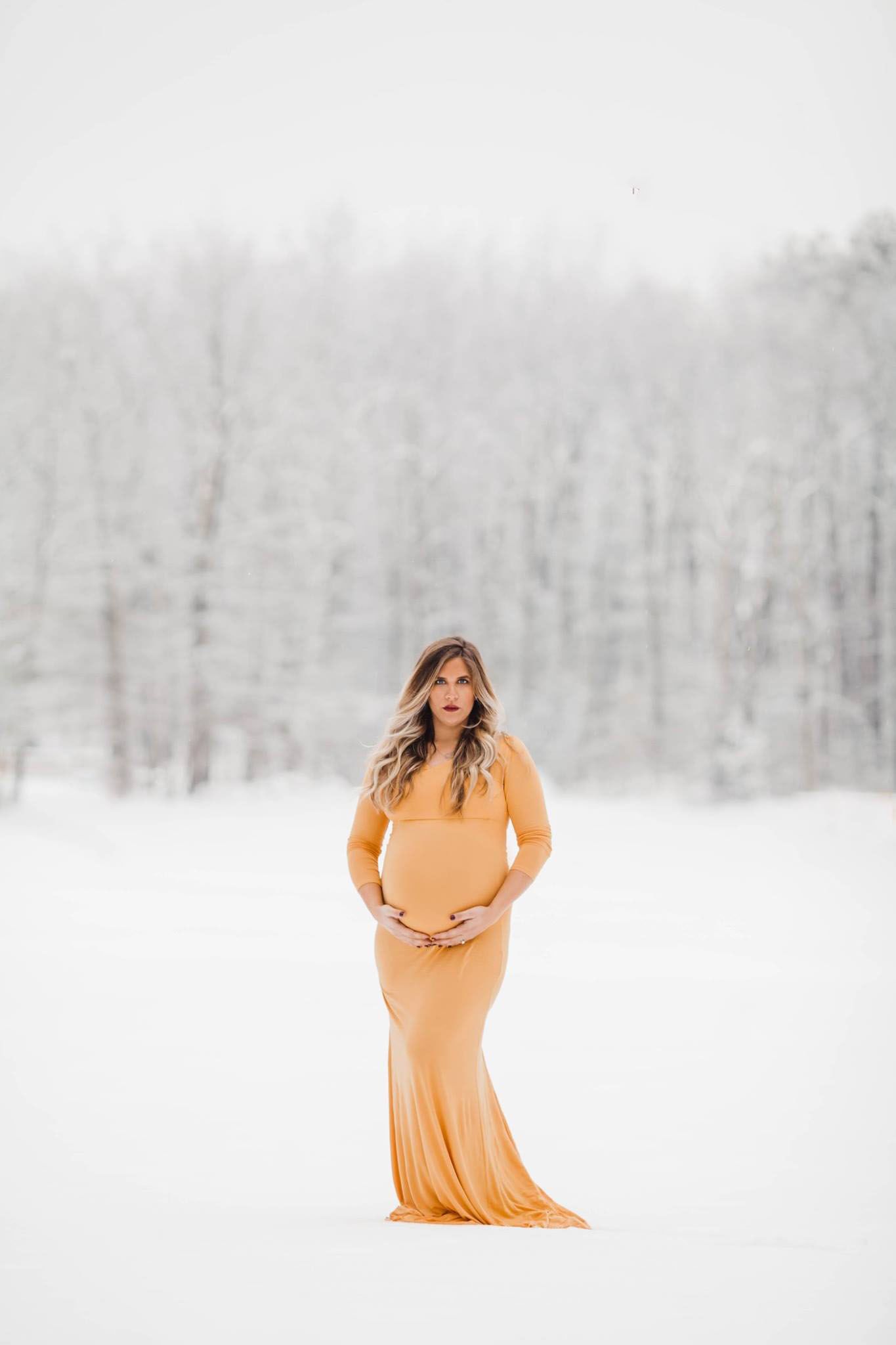 A woman in a peach dress stands in a snowy winter landscape.
