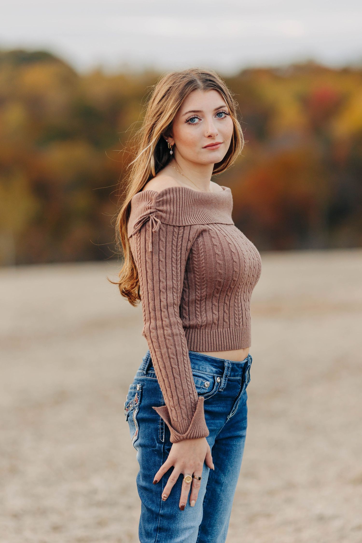 Autumn fashion portrait featuring a brown knit sweater and blue jeans against fall foliage.