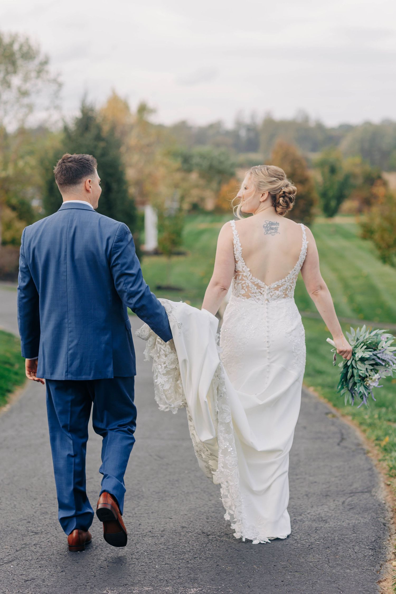A couple walking together on a path with the bride's dress trailing behind them.