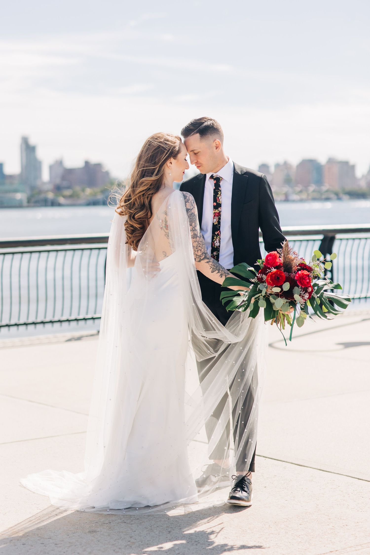 Romantic wedding couple shares intimate moments along a waterfront promenade with city skyline in background.