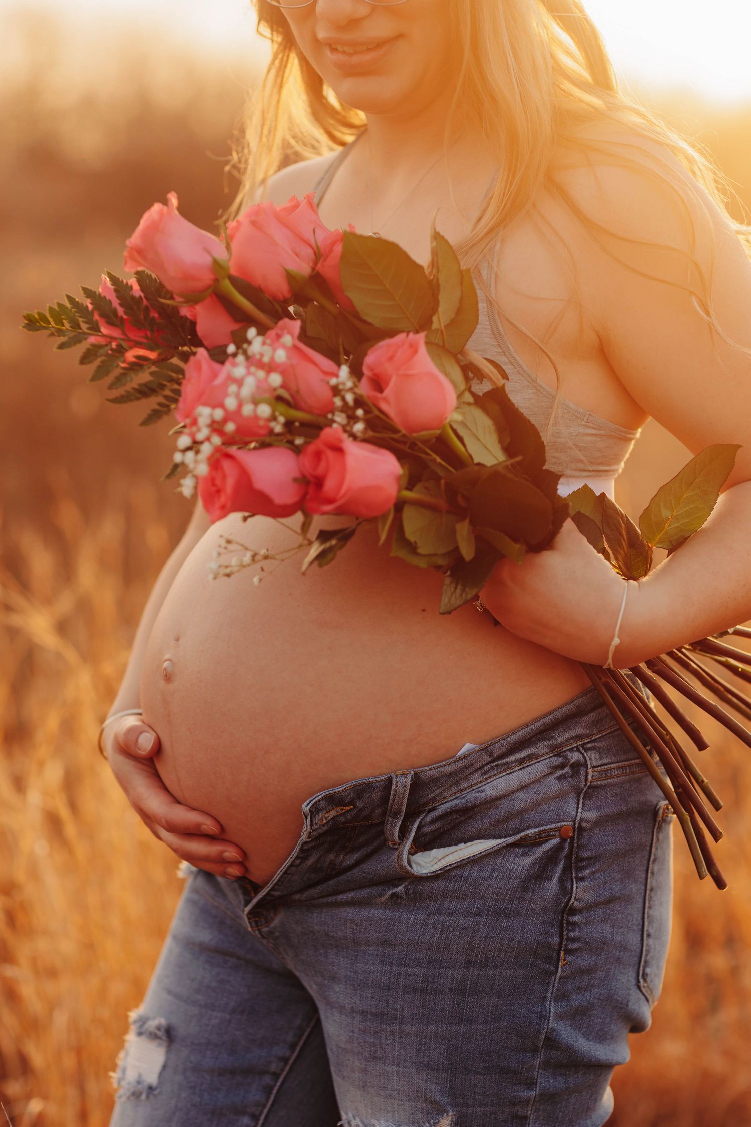 Pregnant woman's belly with pink roses at sunset in golden light.