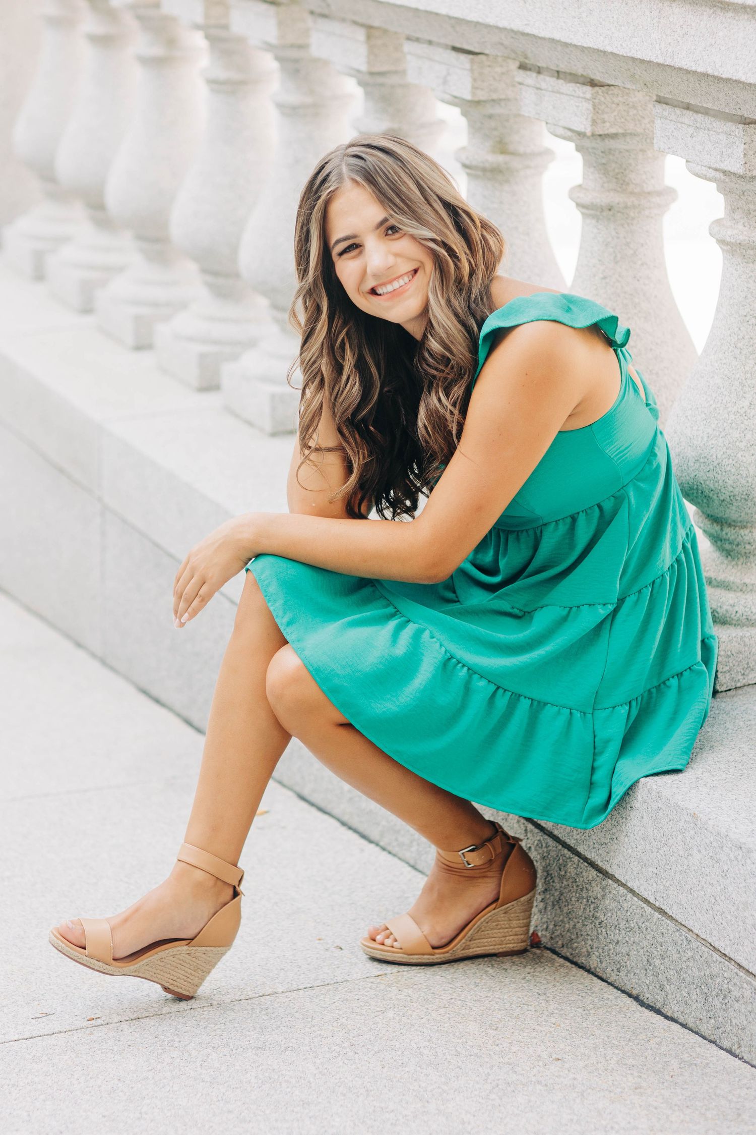 Person in teal dress sitting on white stone steps wearing wedge sandals.