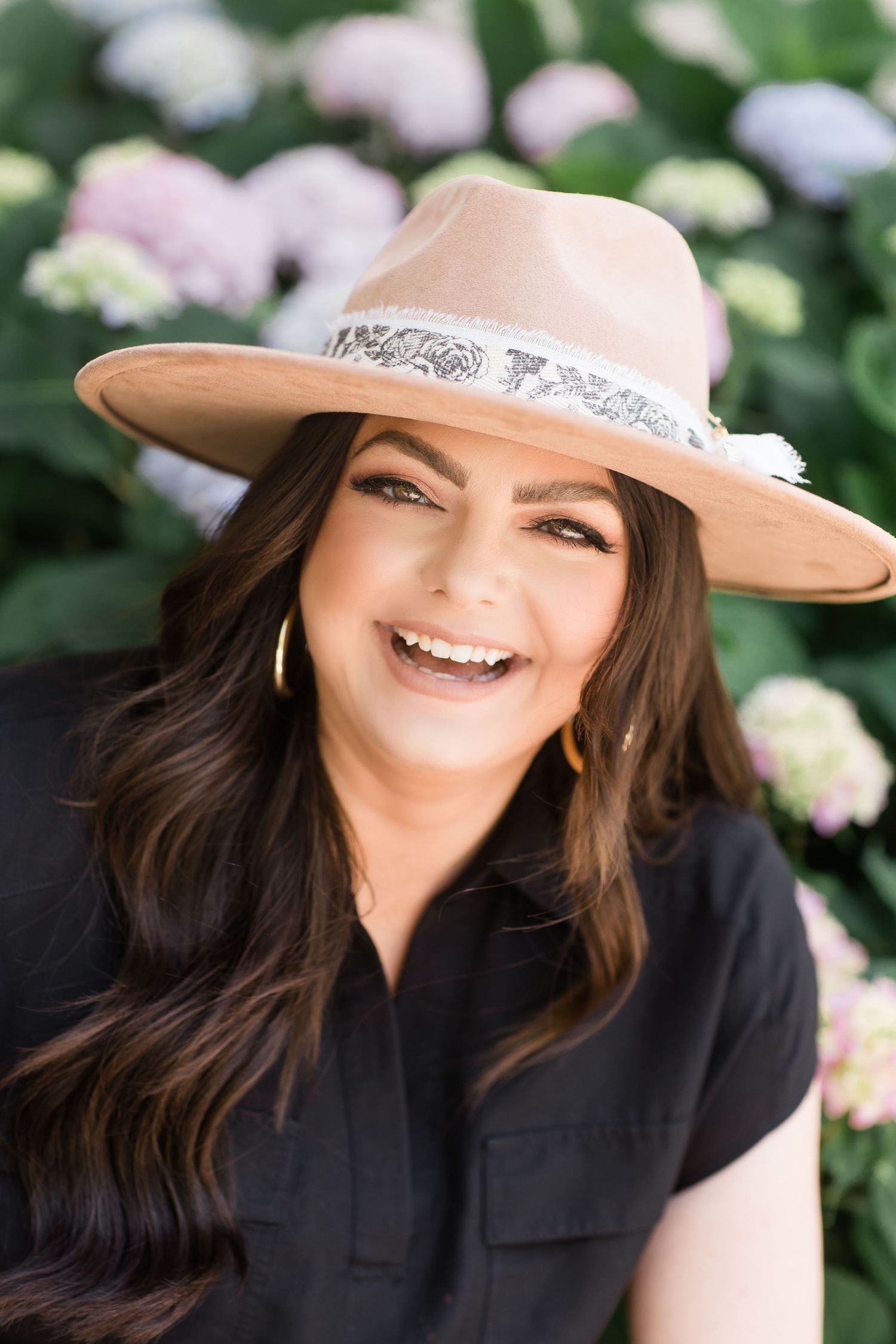 Woman in black shirt and beige hat smiling against floral background.