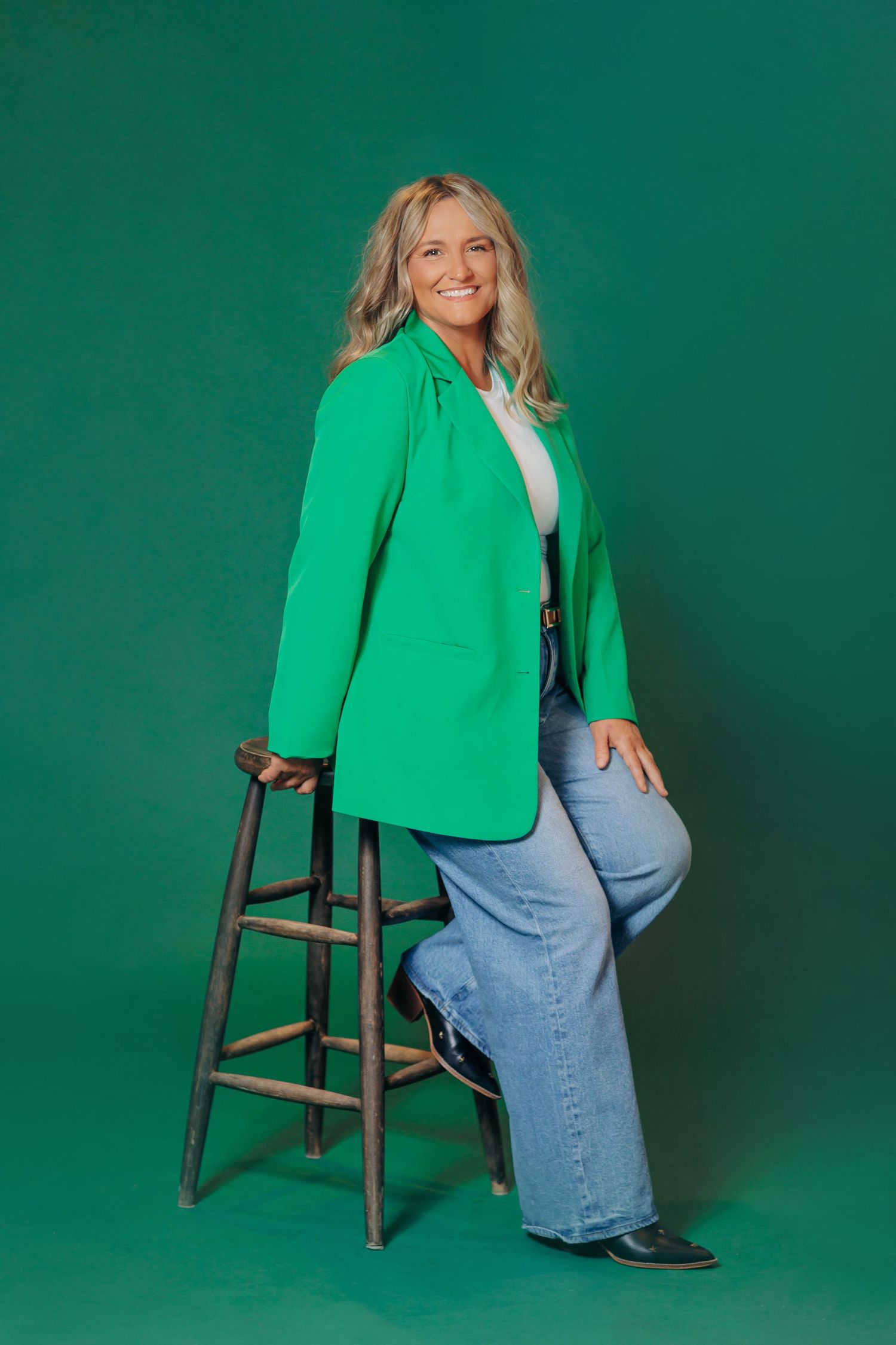 Professional photoshoot against emerald green backdrop featuring bright green blazer and denim.