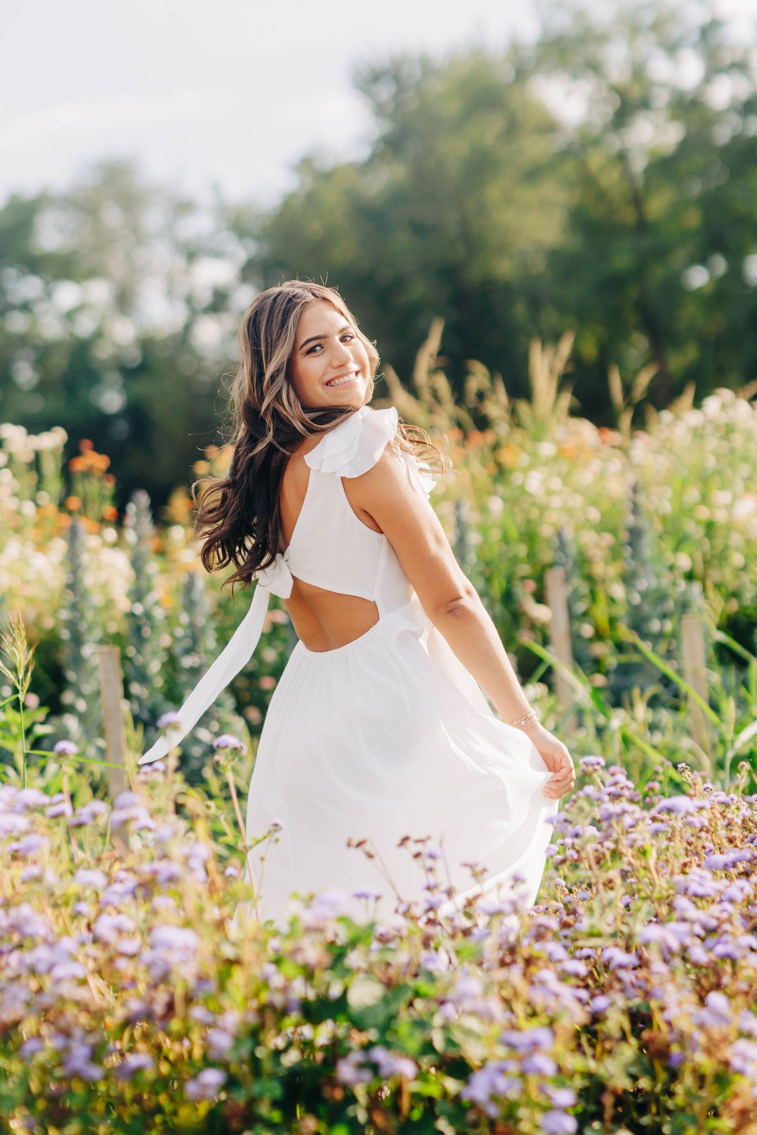 Woman in white dress twirling in a field of purple wildflowers during golden hour.