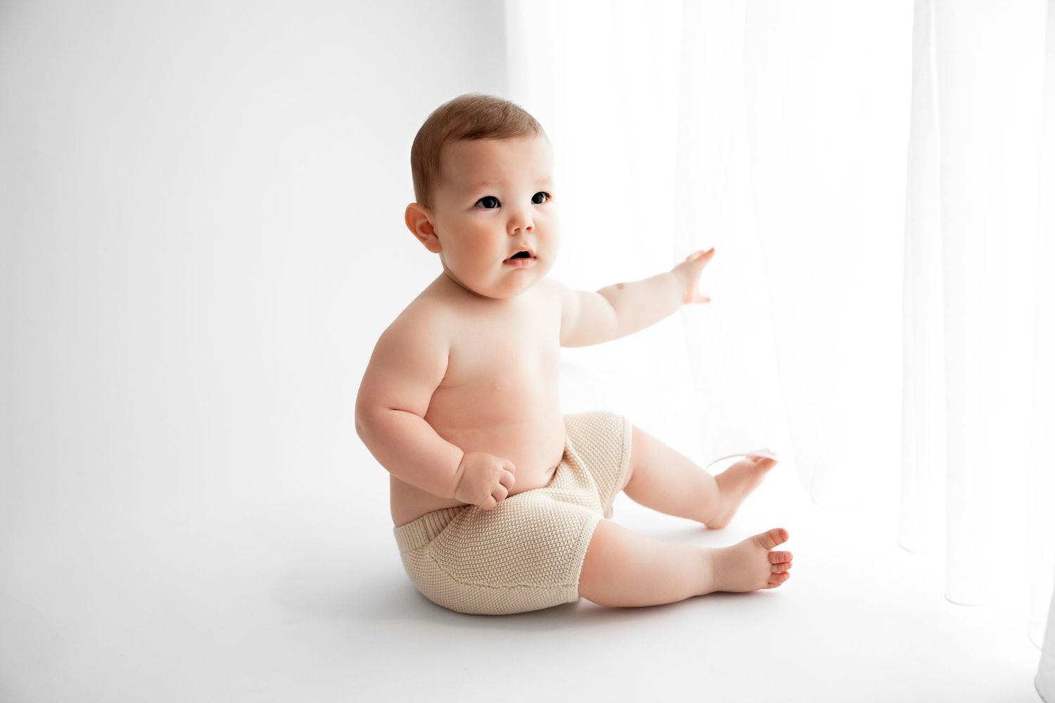 Baby in white diaper sitting and crawling in various poses against white background.