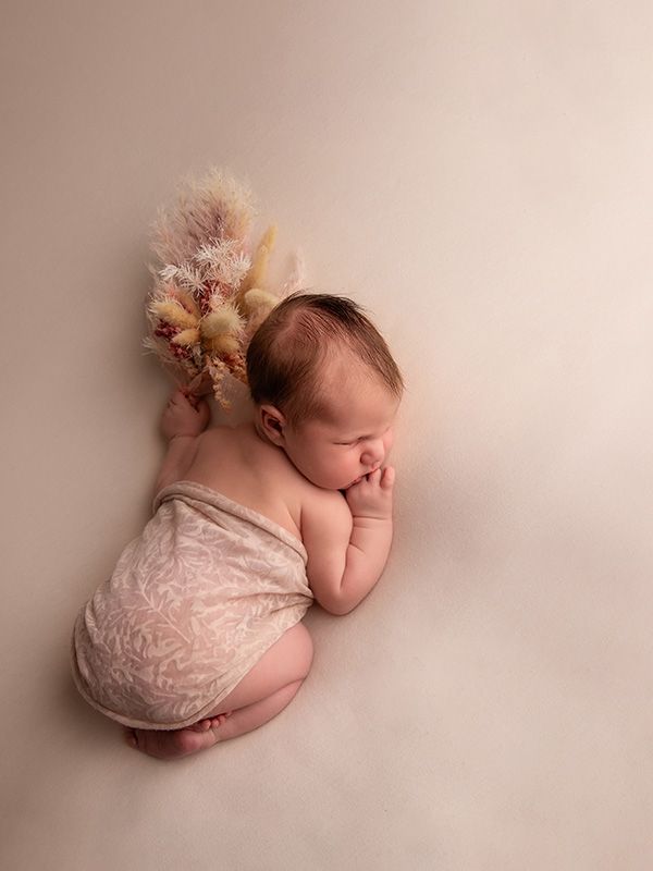 Newborn baby sleeping peacefully in pink lace wrap on neutral backdrop.