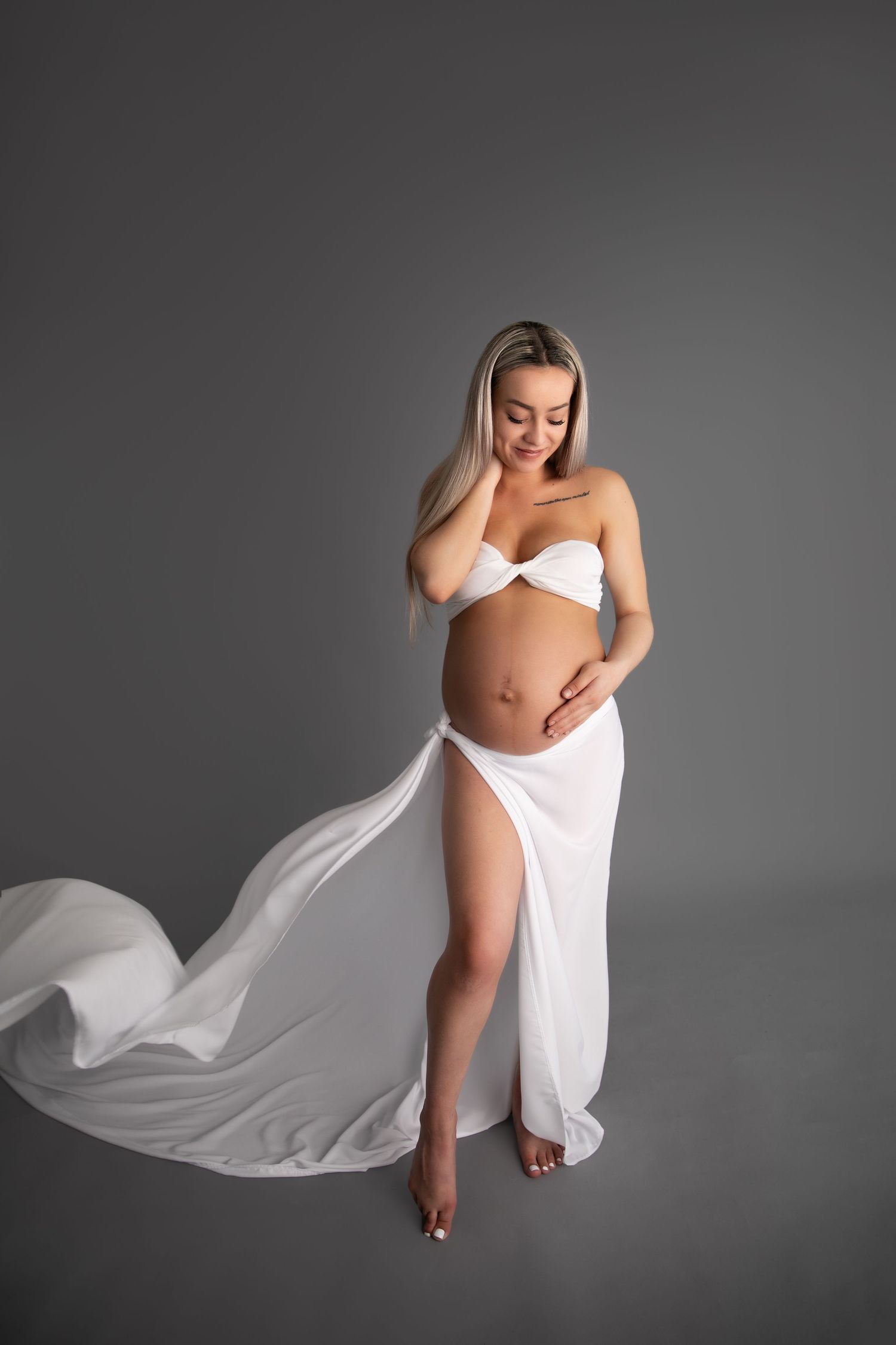 Artistic maternity photo series showing flowing white fabric against dark background in four elegant poses.