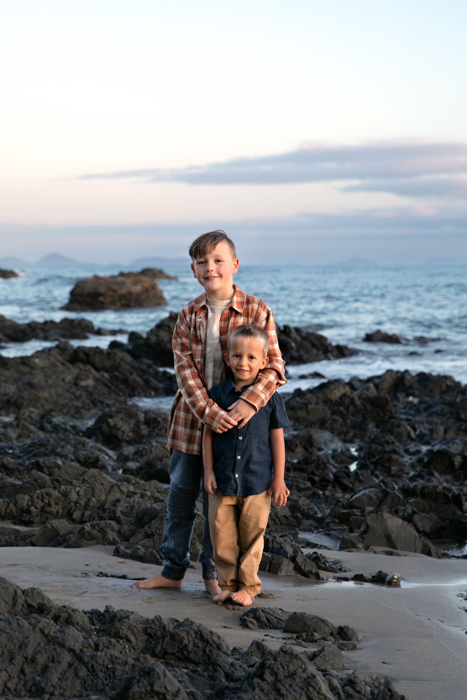 Two children playing and posing together on rocky beach at sunset.