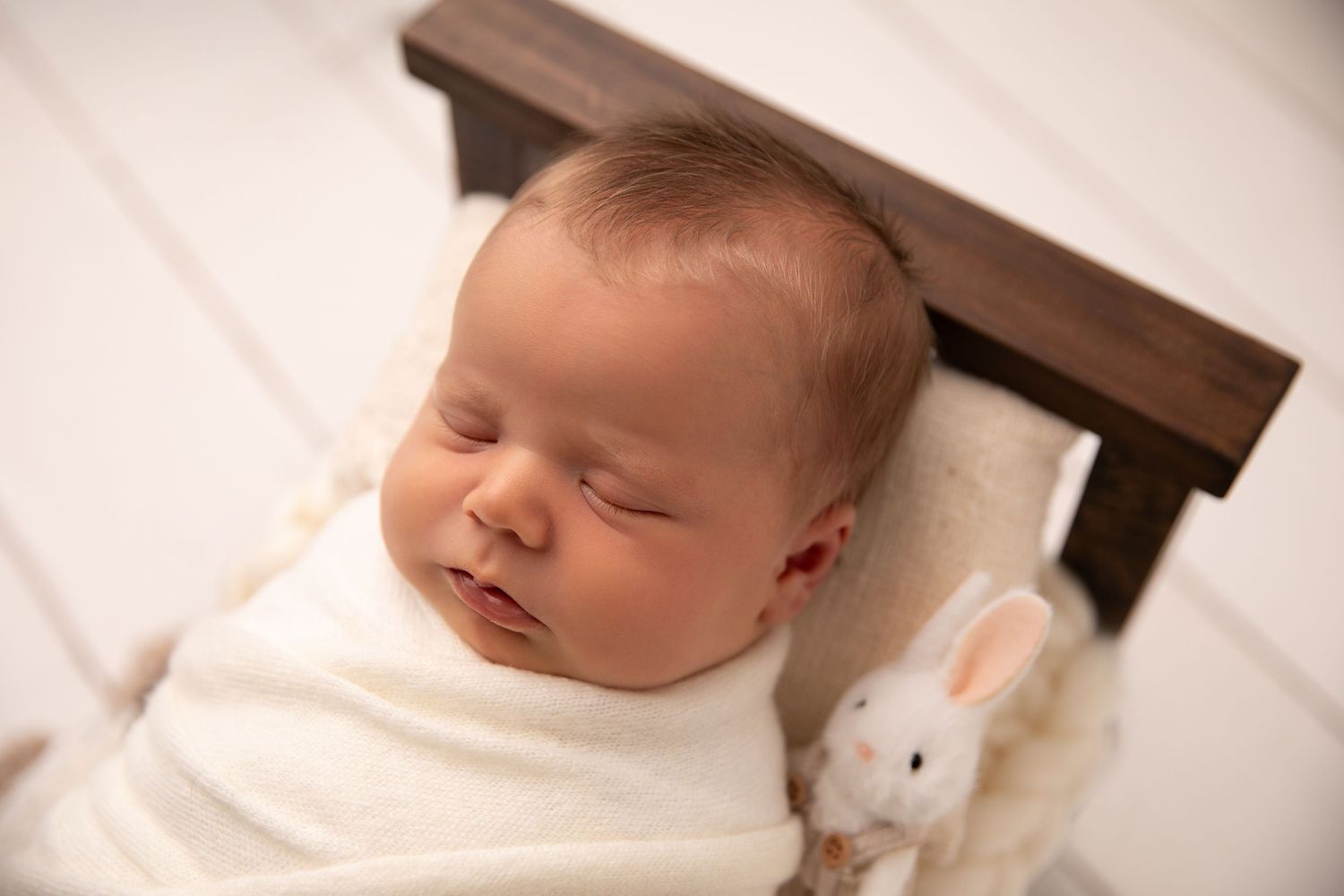 Sleeping newborn baby swaddled in white blanket rests peacefully in wooden crib.