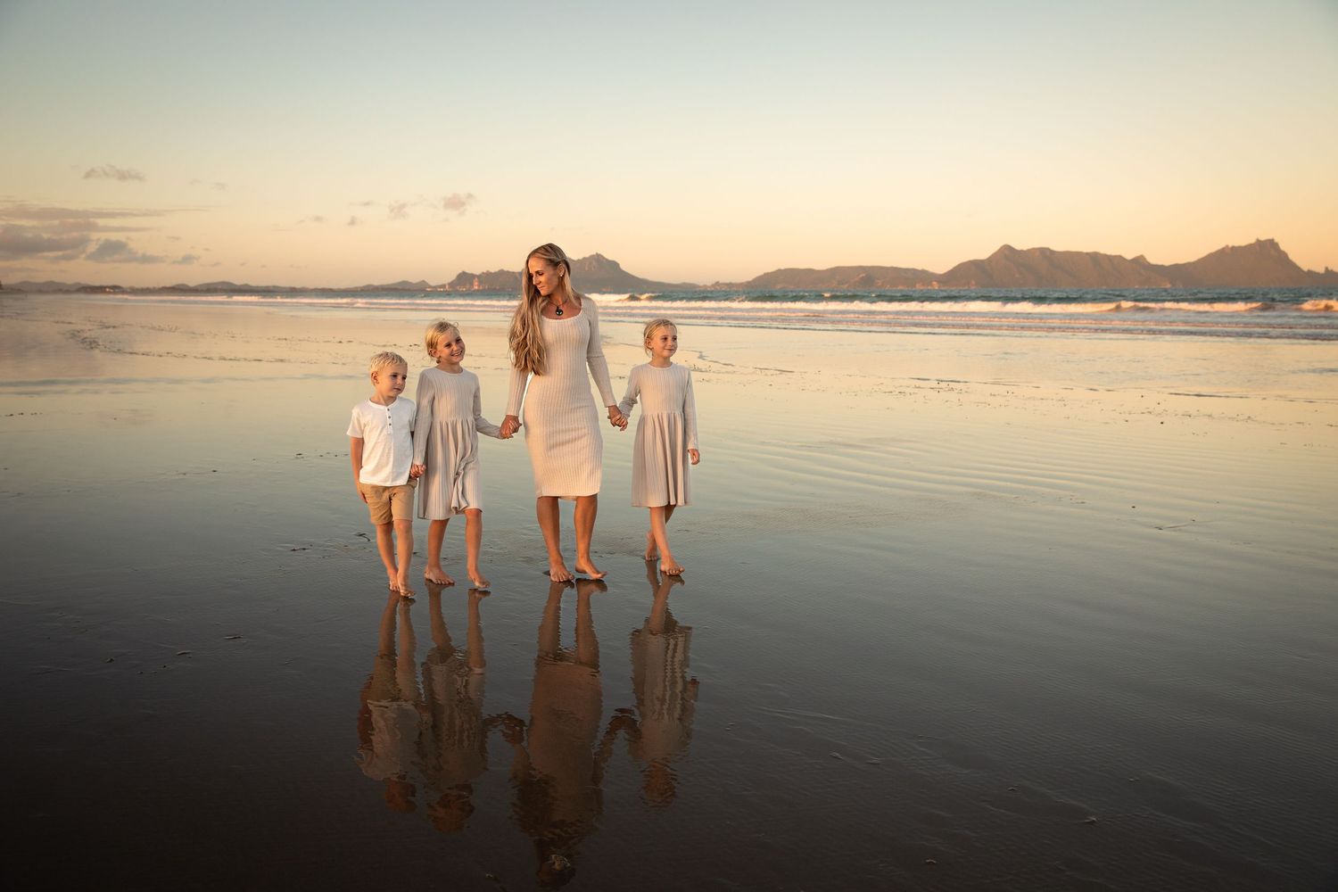 A group stands together at sunset on a reflective beach with mountains in the distance creating a serene silhouette.