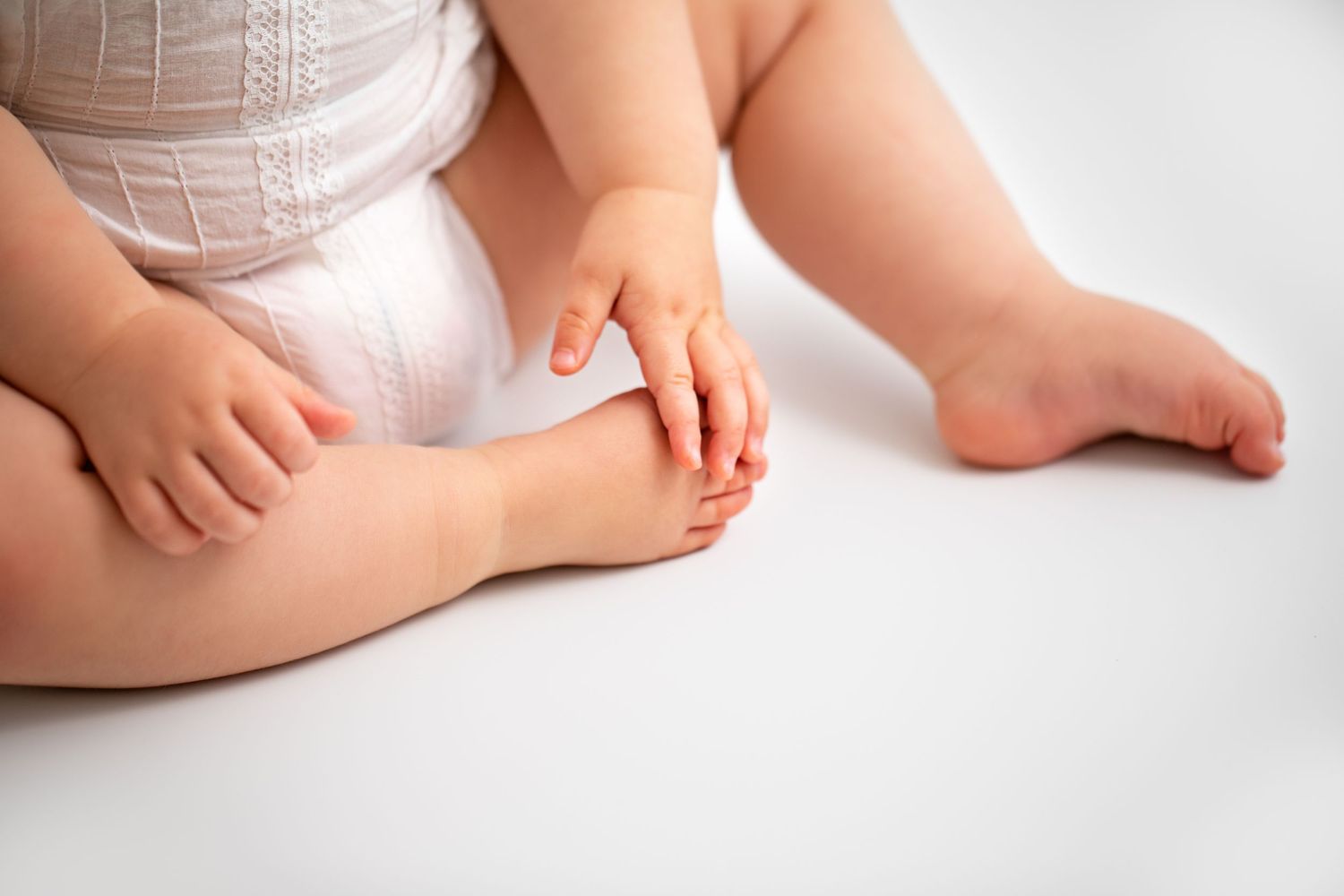 Close-up view of baby feet and hands against a white background showing delicate skin texture and tiny fingers and toes.