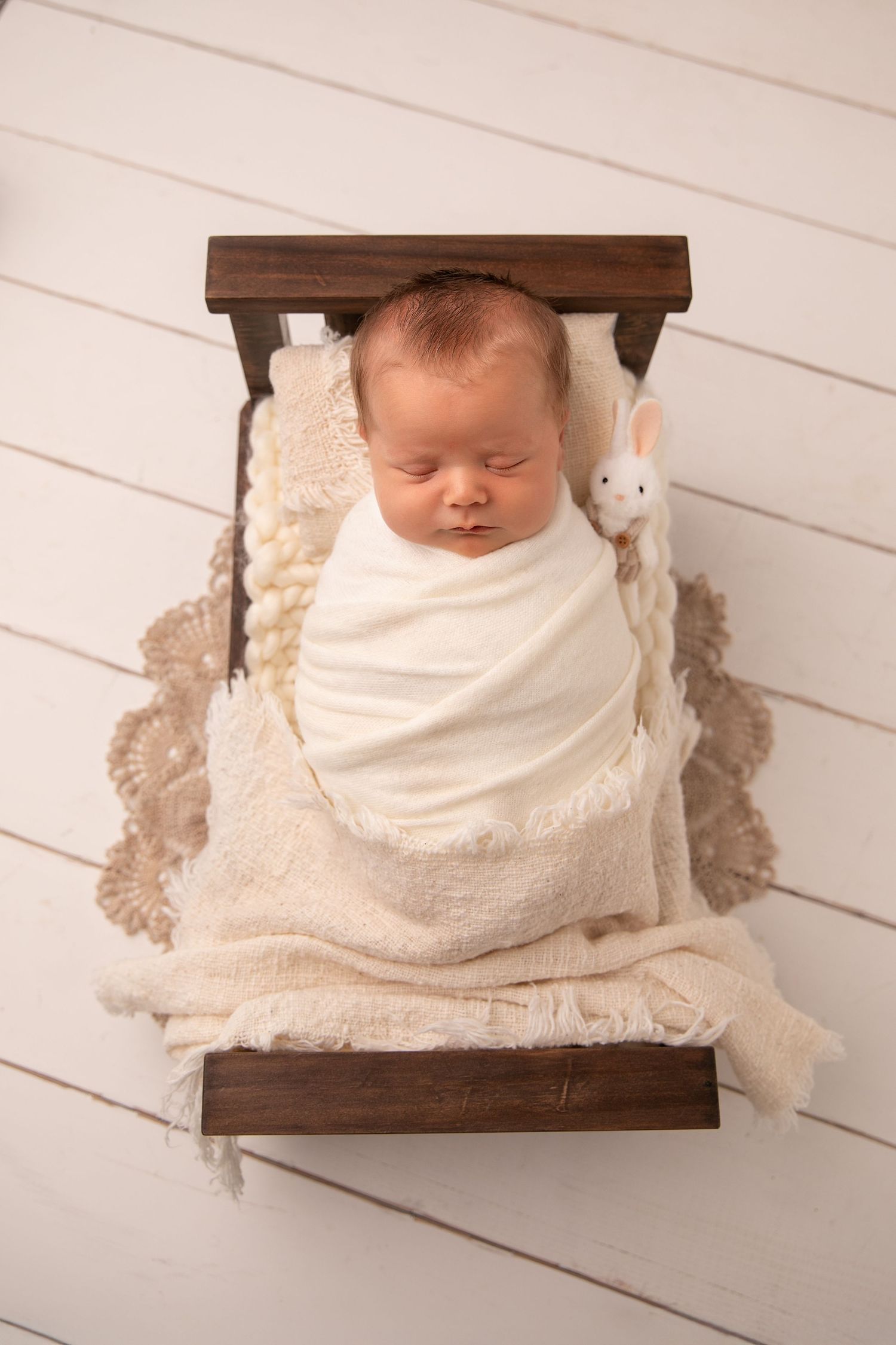 A newborn baby sleeping peacefully on a wooden prop against a white wooden backdrop in a series of similar photos.