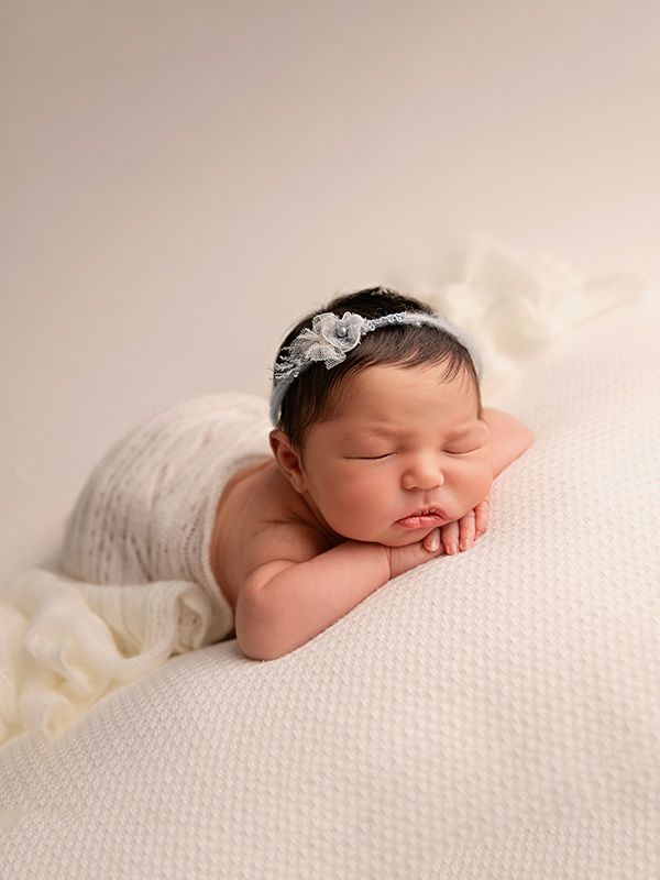 A sleeping newborn baby rests peacefully on a textured white blanket in a professional studio portrait setting.