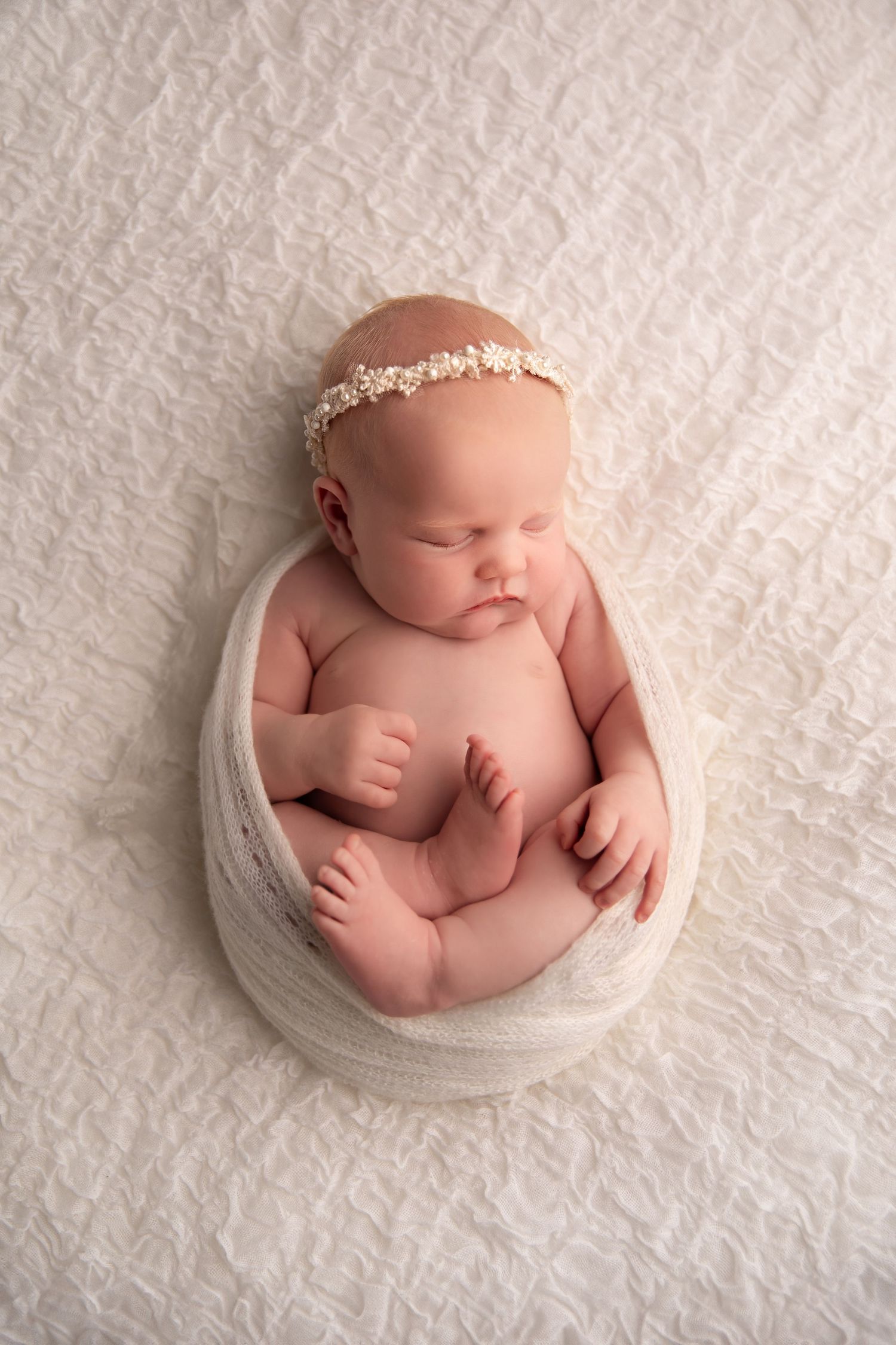 Newborn baby photography series showing peaceful sleeping infant in white wrap against textured white backdrop.