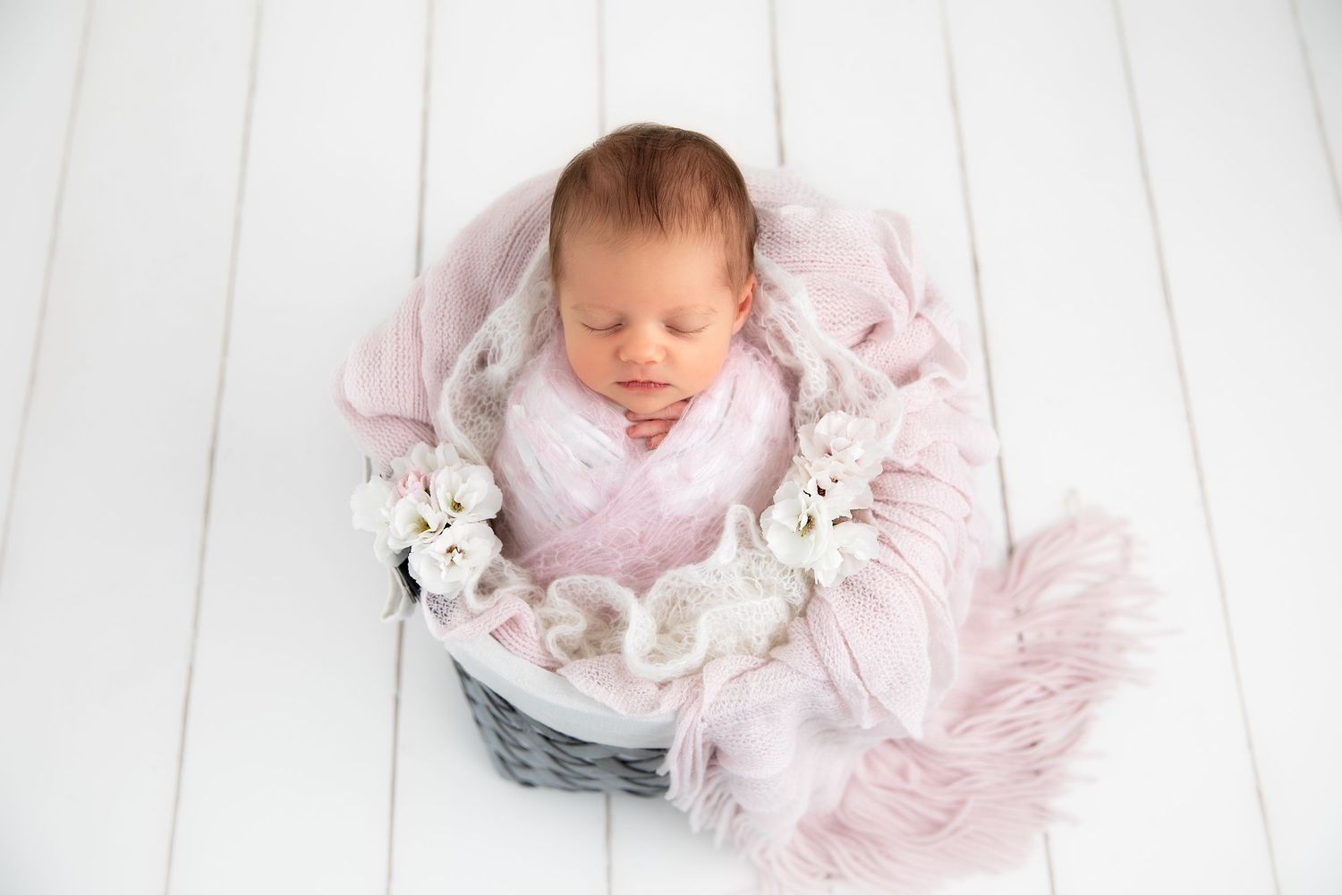 Newborn baby wearing pink sleeps peacefully on white wooden floor with soft plush bunny toy.
