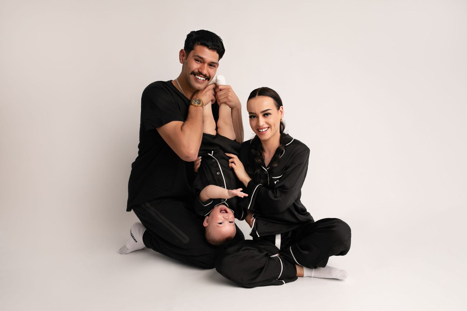 A family in matching black outfits sits together on white backdrop for a minimalist portrait session.