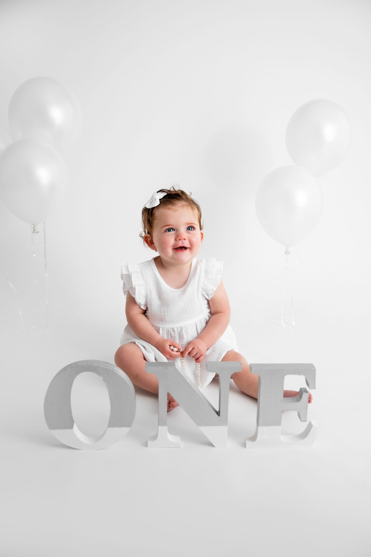 A baby in white clothing crawls and plays with large decorative letters against a bright white background.