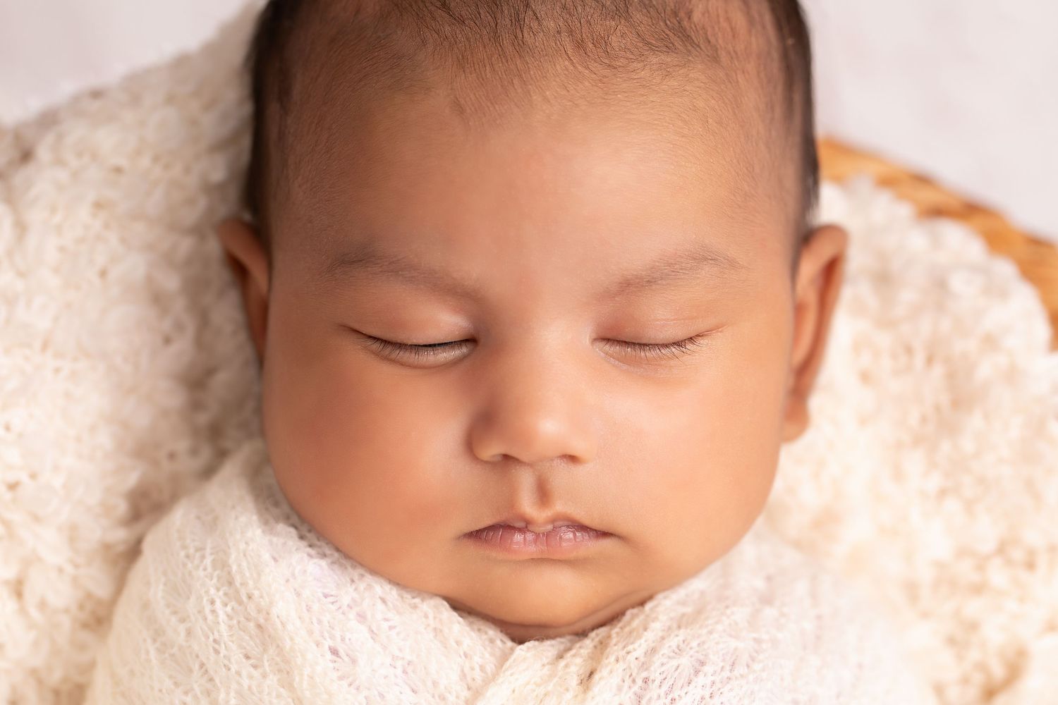 Sleeping newborn baby rests peacefully on soft cream-colored blanket with delicate lighting.