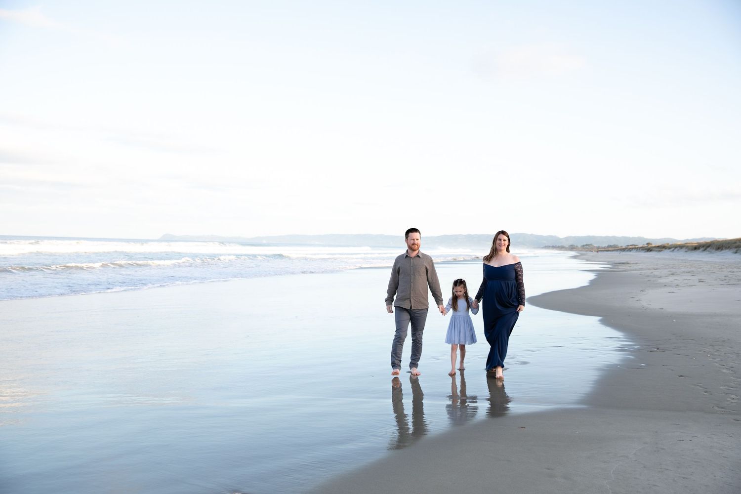 People walking together along a peaceful beach shoreline at sunset with waves gently rolling in.