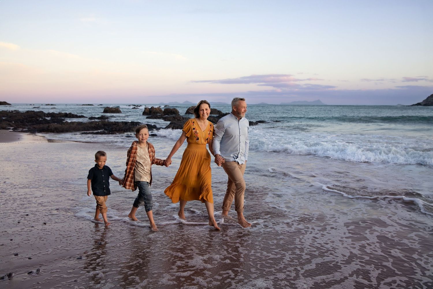A group of people playing and splashing in the shallow ocean waves at sunset along a sandy beach.