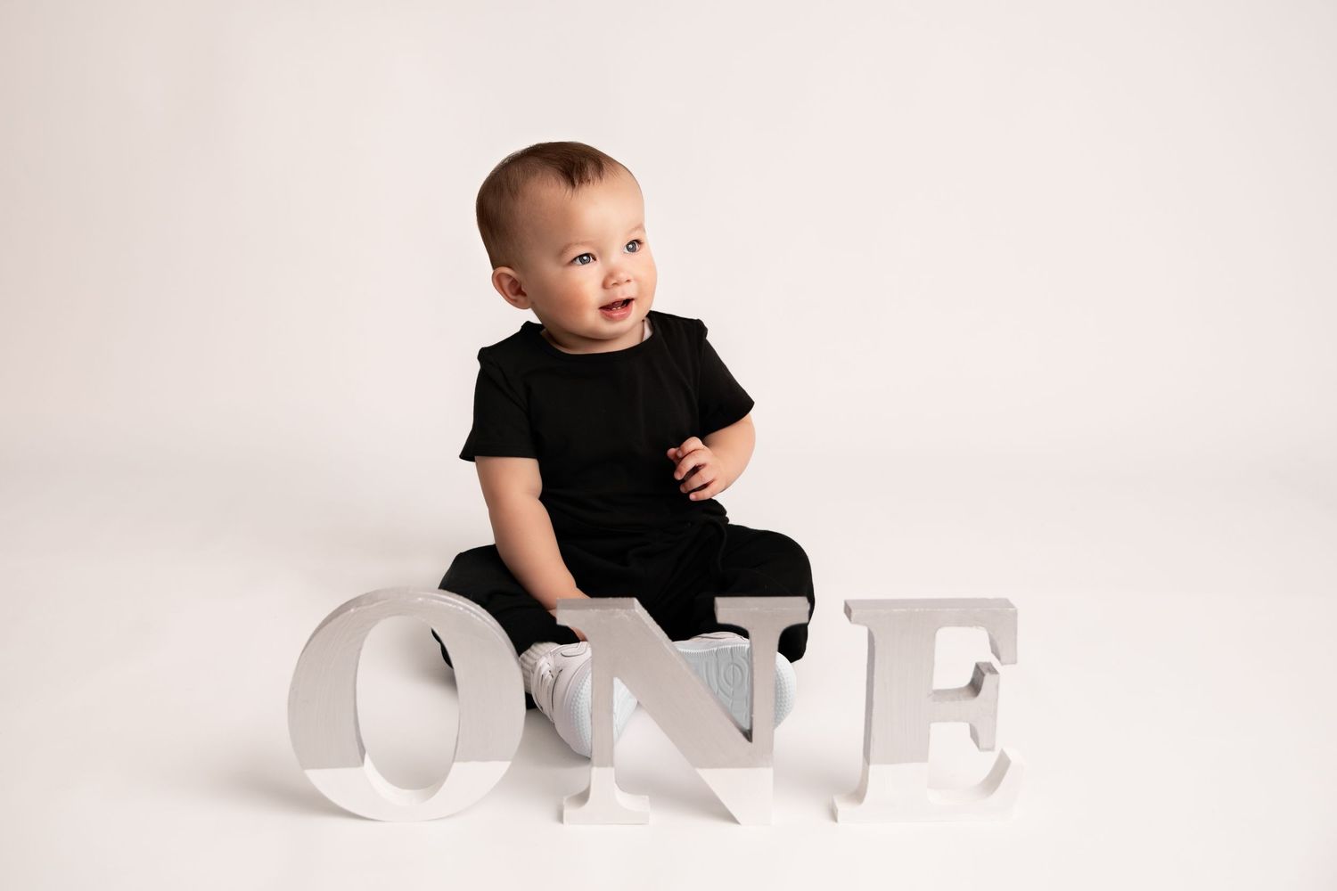 A baby in a black shirt sits on a white background with large white letters spelling STOP.