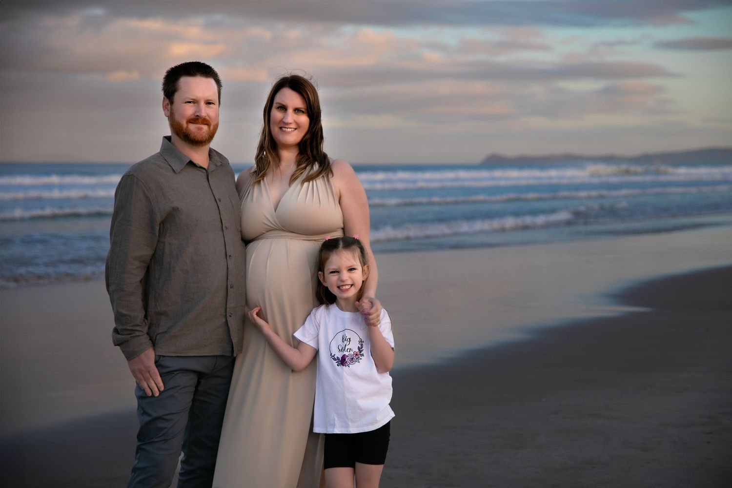 A group poses together at sunset on a scenic beach with waves and cloudy skies in the background.