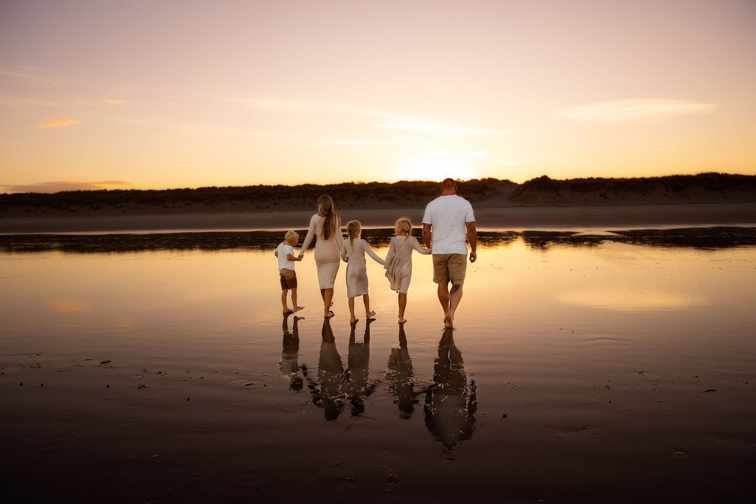 Silhouettes of people walking along a beach at sunset with reflections in the water creating a mirror effect.