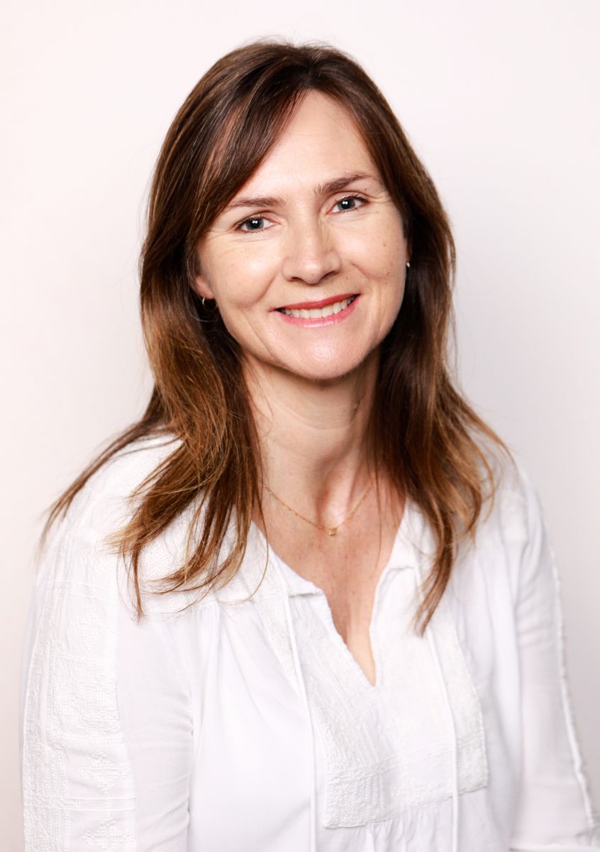 Professional portrait of a woman wearing a white blouse smiling against a neutral background.