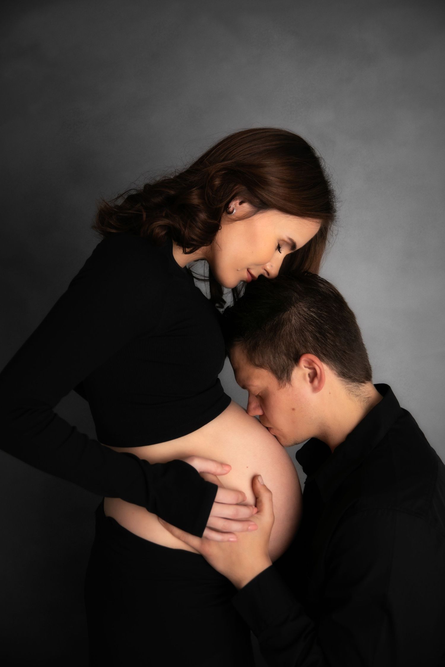 A dramatic black and white photo series showing a couple in dark clothing embracing in silhouette against a gray background.